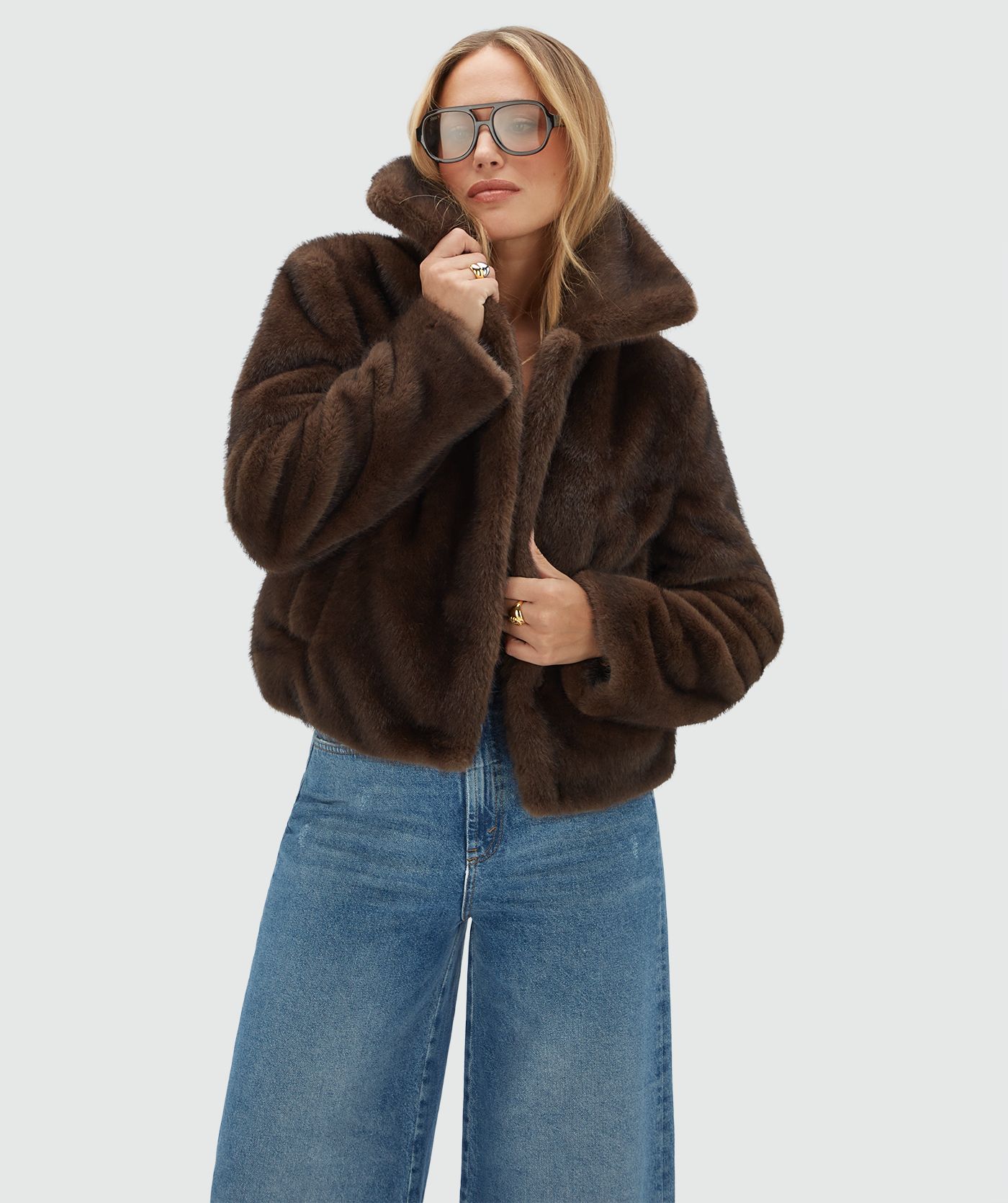 Model draagt een donkerbruine bond jas gecombineerd met een jeans en een donkerbruine zonnebril.