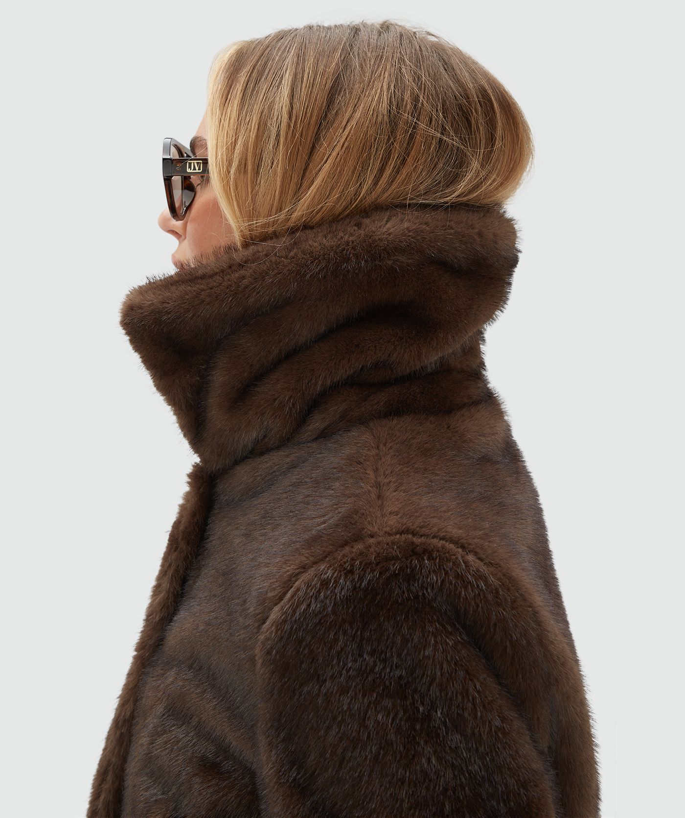 Model draagt een donkerbruine bond jas met een lichtbruine lak look broek.