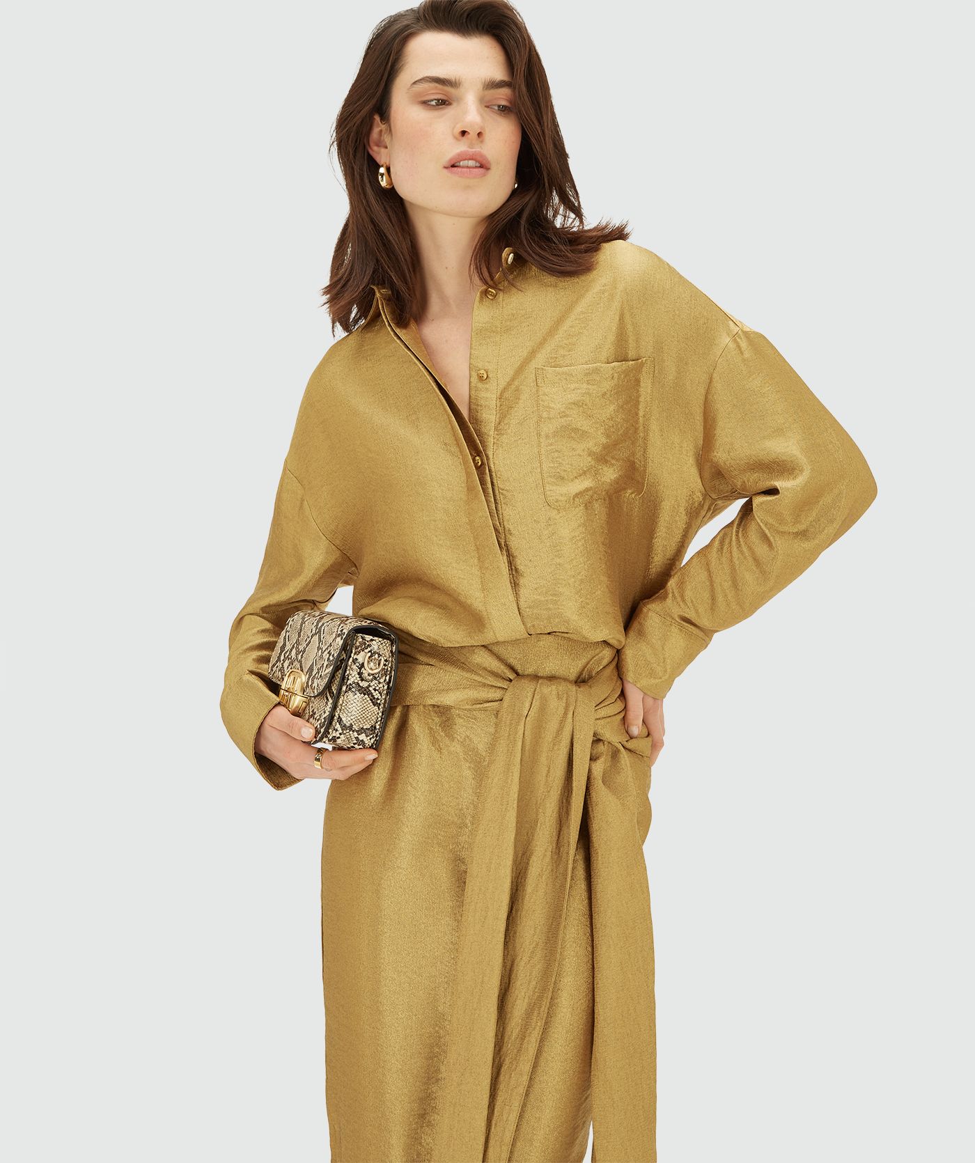 Model draagt een Dark Gold blouse met lange mouwen, knoopsluiting en een borstzak. De blouse heeft een glans