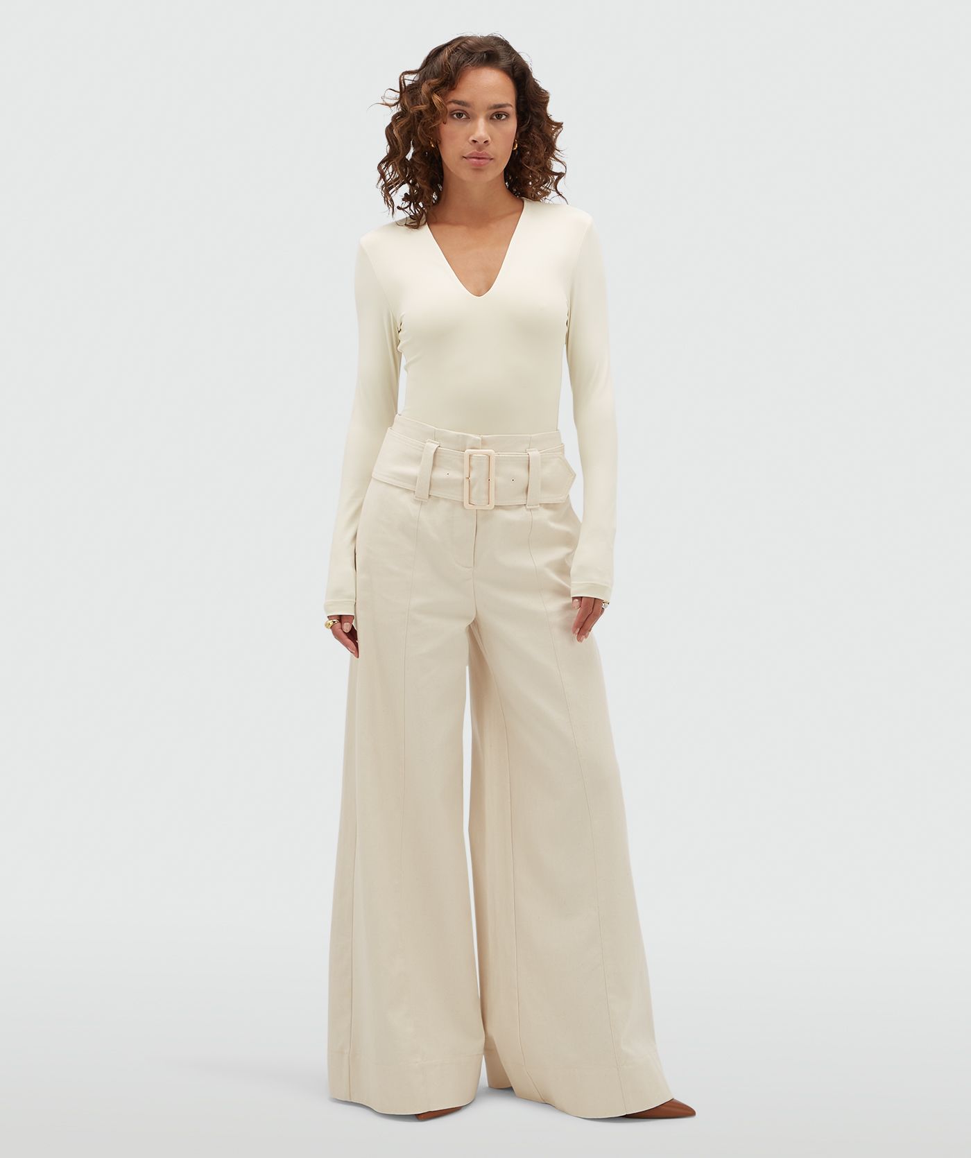 Model draagt gebroken witte high waisted wide leg jeans met een grote riem.