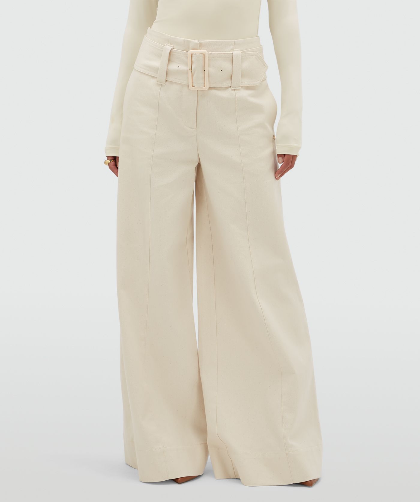 Model draagt gebroken witte high waisted wide leg jeans met een grote riem.