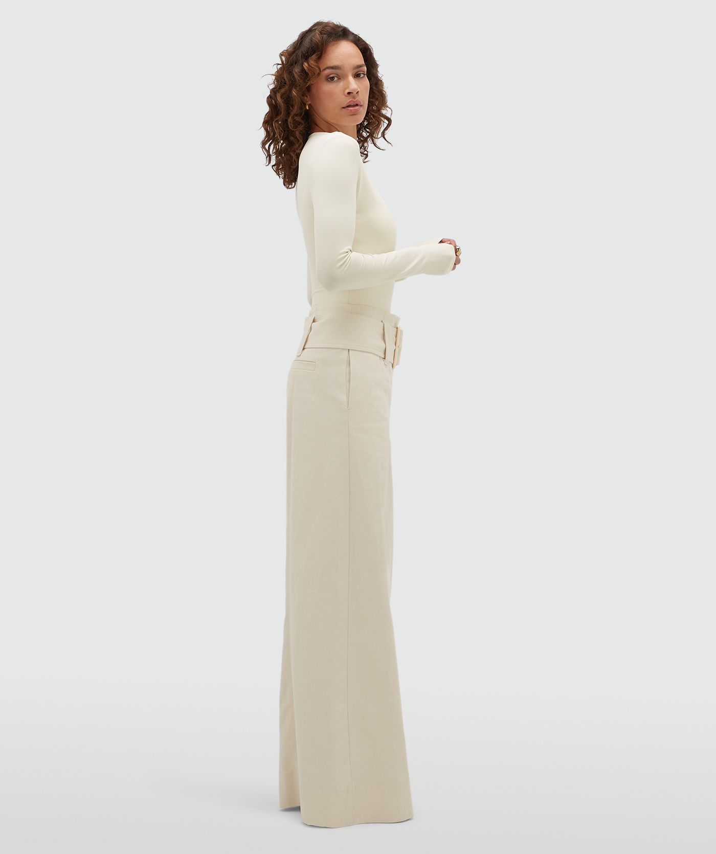Model van opzij in een gebroken witte high waisted wide leg jeans met een grote riem.