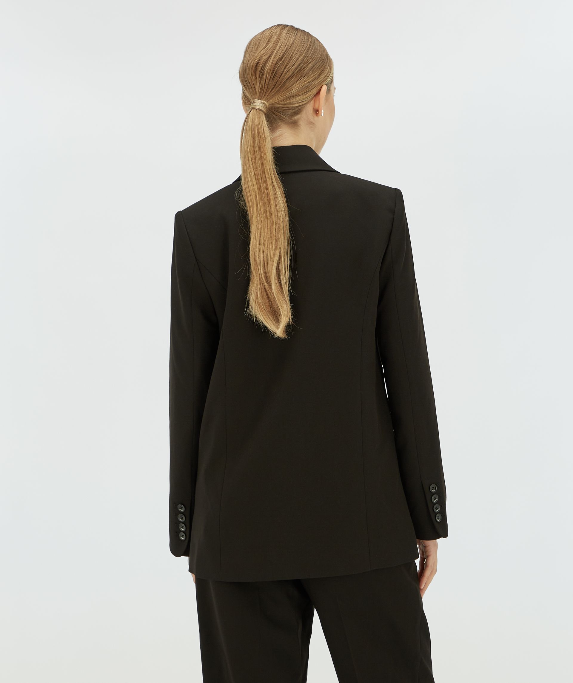 Achteraanzicht van een model die een zwarte blazer draagt.