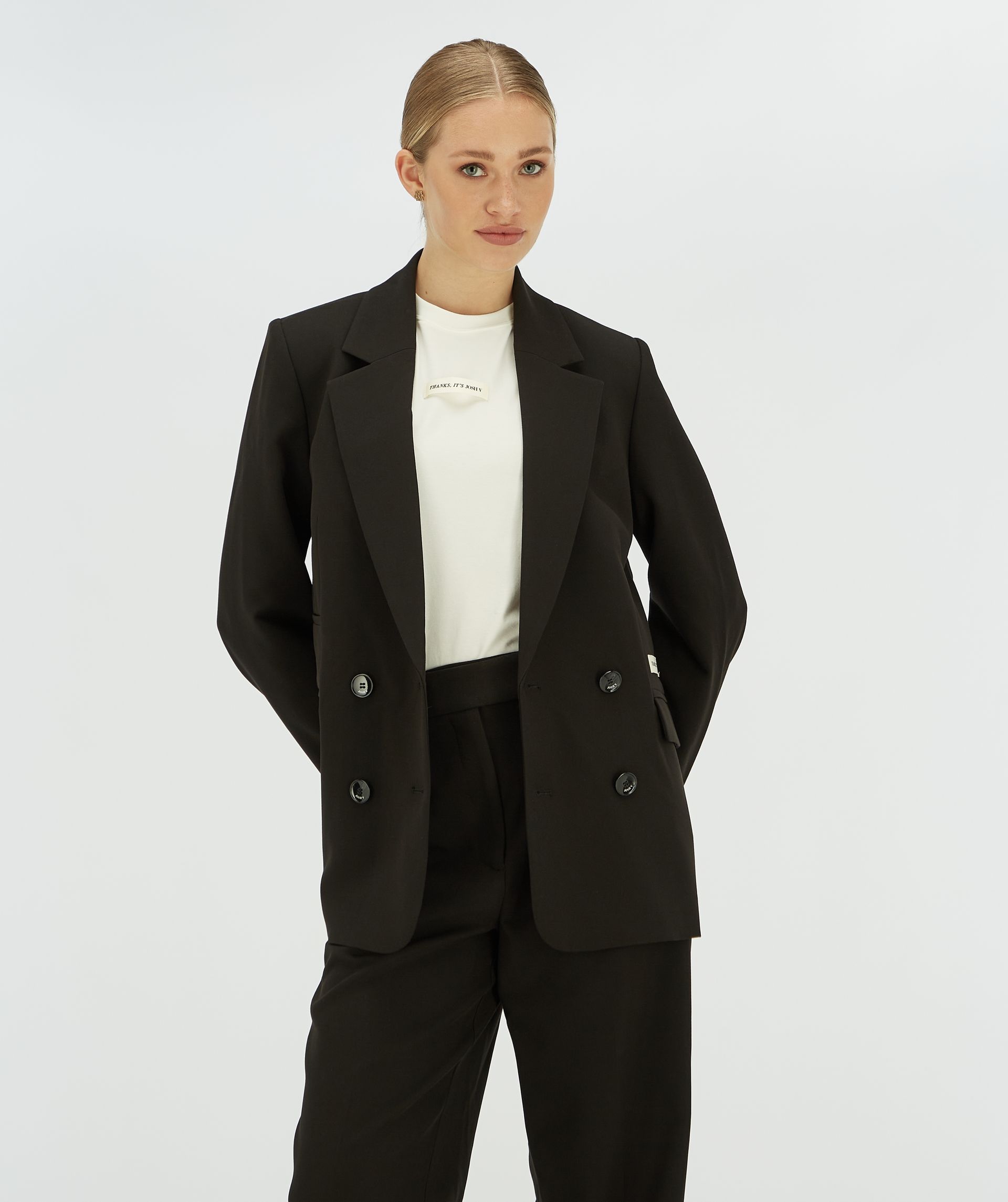 Model draagt een zwarte blazer met aan de zijkant een Josh v label.