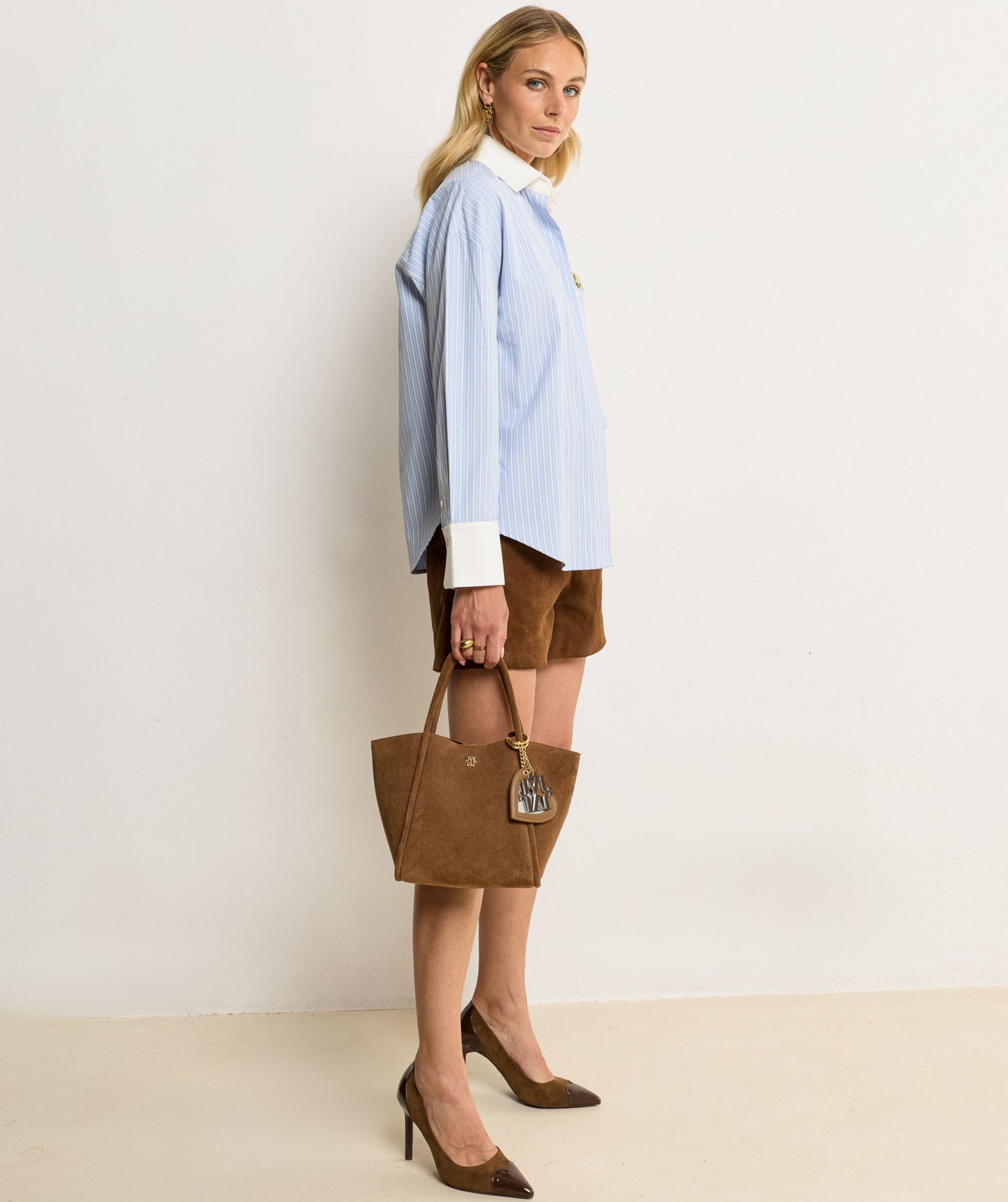 Model draagt een Brown Dark Brown pump met hoge hak, uitgevoerd in een combinatie van suède en glanzend lakleer