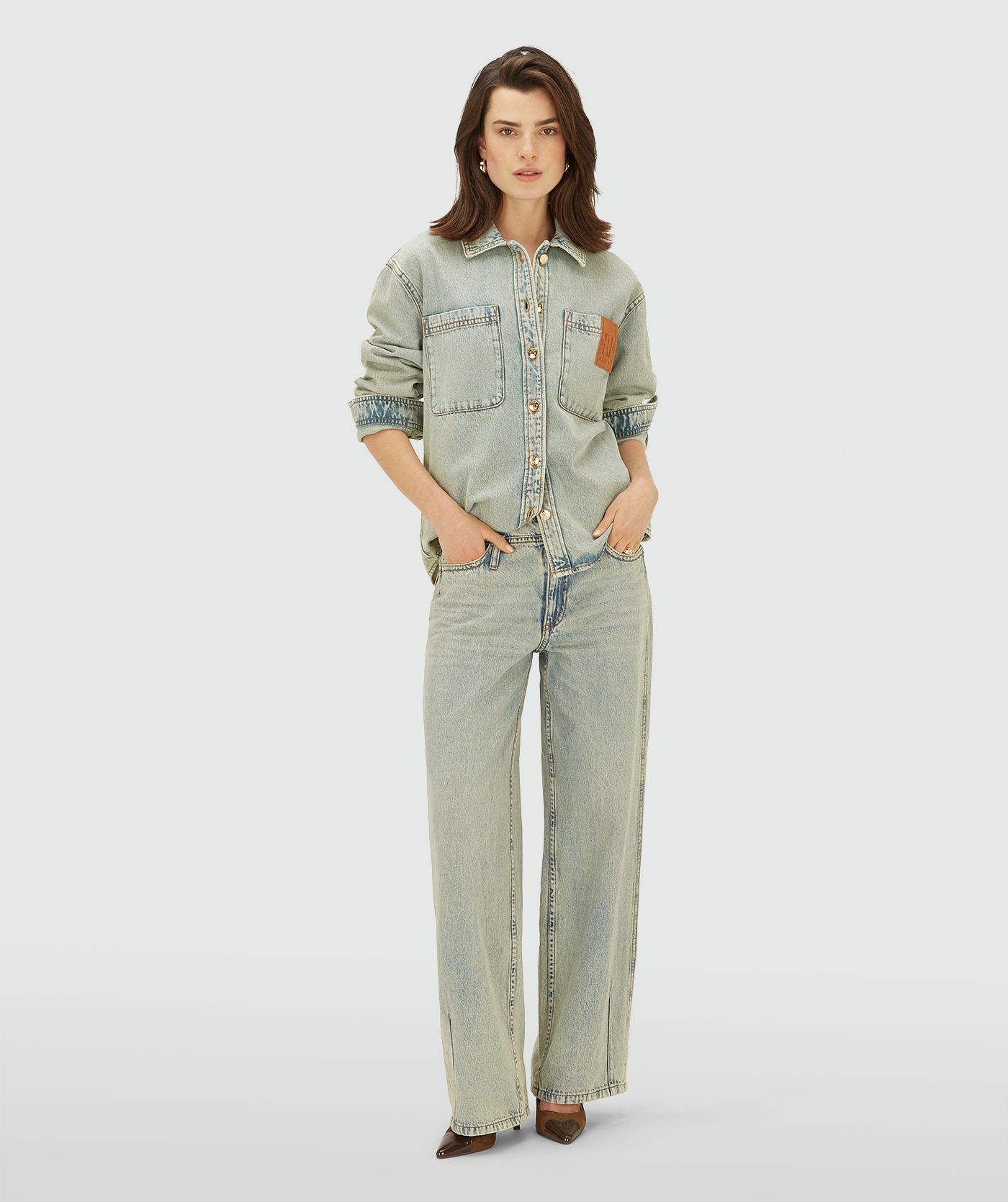 Model draagt een light Dirty Denim blouse met knoopsluiting en borstzakken. De blouse heeft een relaxed fit en een leren logo-detail op de borst