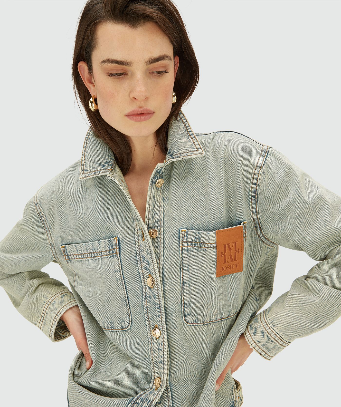Model draagt een light Dirty Denim blouse met knoopsluiting en borstzakken. De blouse heeft een relaxed fit en een leren logo-detail op de borst