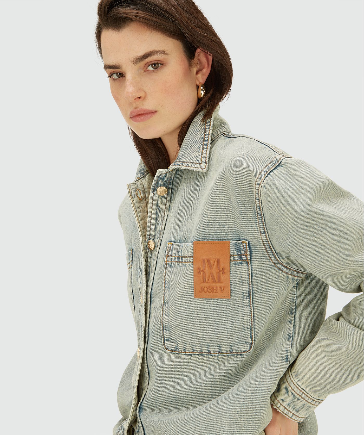 Model draagt een light Dirty Denim blouse met knoopsluiting en borstzakken. De blouse heeft een relaxed fit en een leren logo-detail op de borst