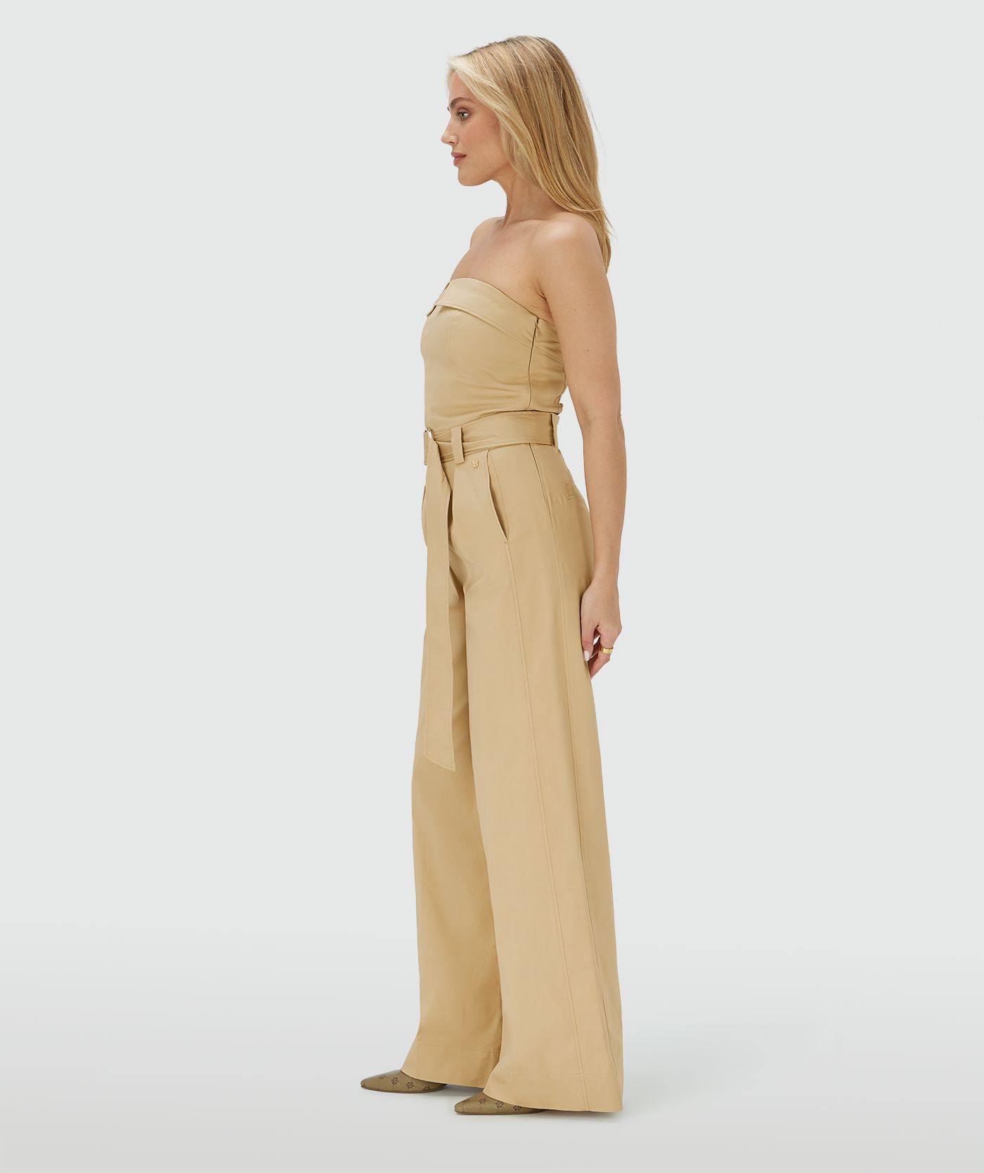Zijaanzicht van een model in een wide leg jumpsuit in de kleur Light Camel met een gespdetail in de taille
