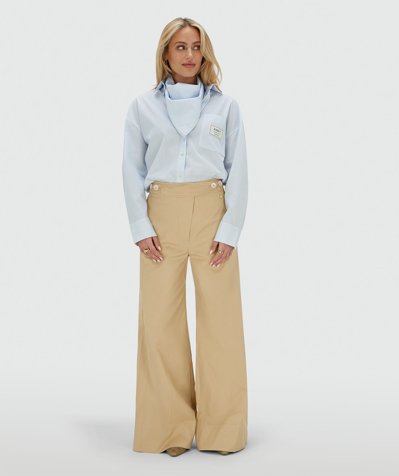 Het model draagt een oversized blauwe blouse met borstzak, inclusief het bijpassende sjaaltje