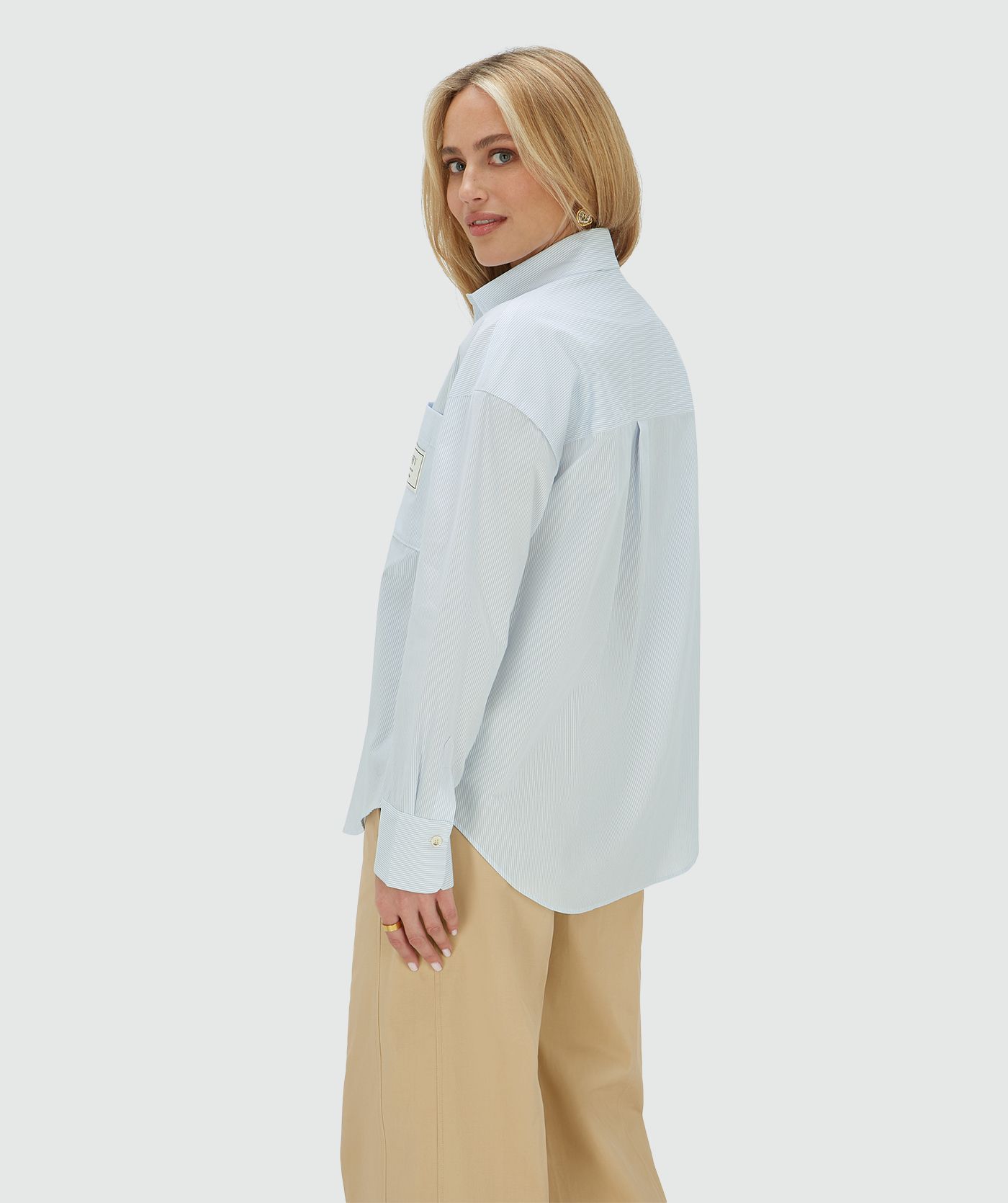 Model van opzij in een oversized blauwe blouse met borstzak, exclusief het bijpassende sjaaltje