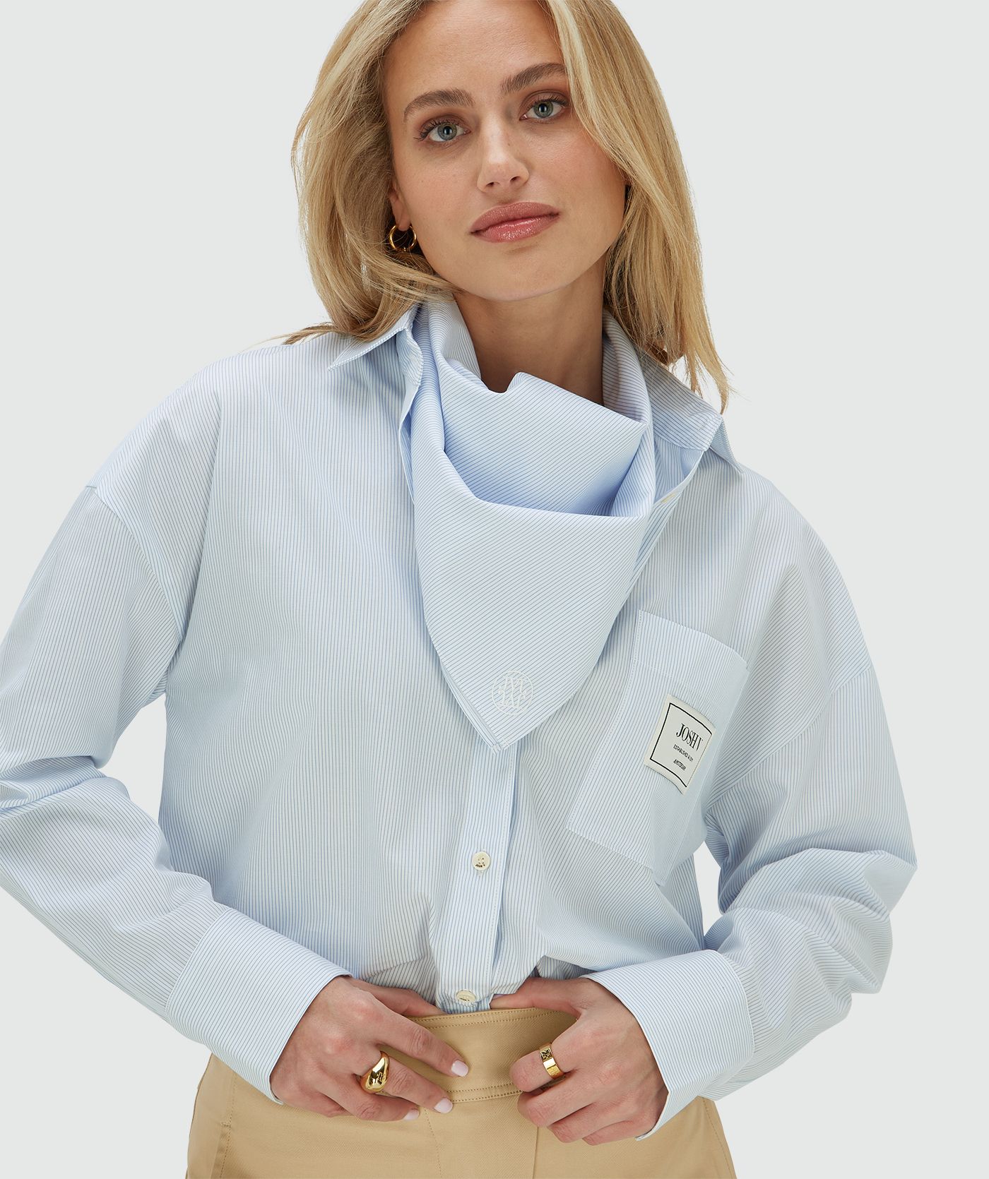 Het model draagt een oversized blauwe blouse met borstzak, inclusief het bijpassende sjaaltje