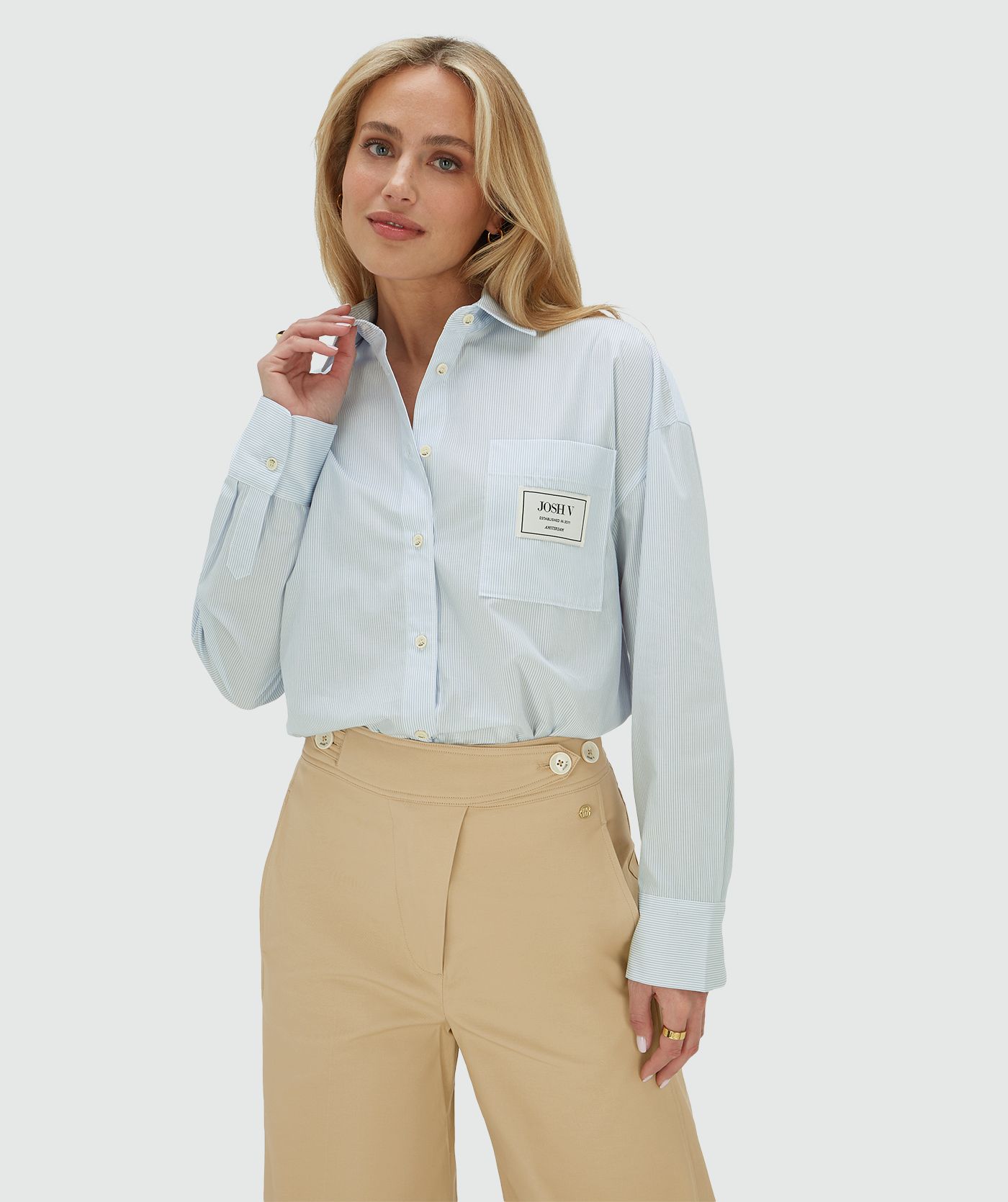 Het model draagt een oversized blauwe blouse met borstzak, exclusief het bijpassende sjaaltje