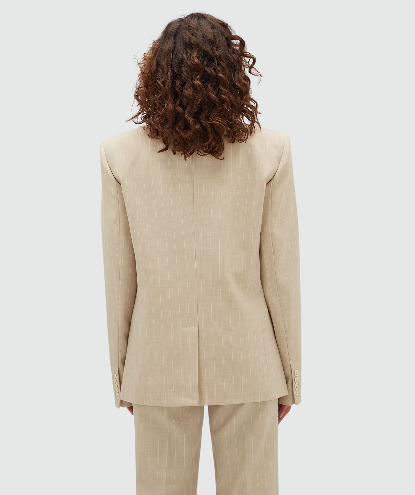 Achteraanzicht van een model in een oversized beige blazer met een krijtstreepje.