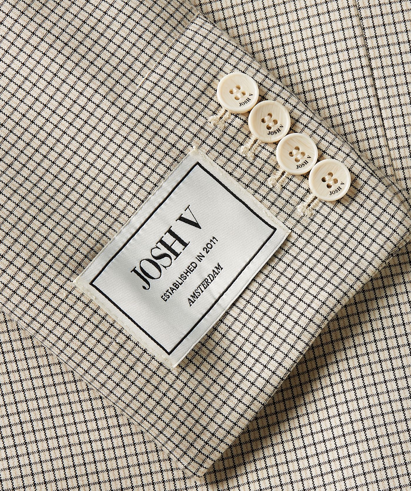 Close-up van een oversized blazer in het Stone Check-patroon, waarbij het JOSH V-label met knoopjes op de mouw zichtbaar is