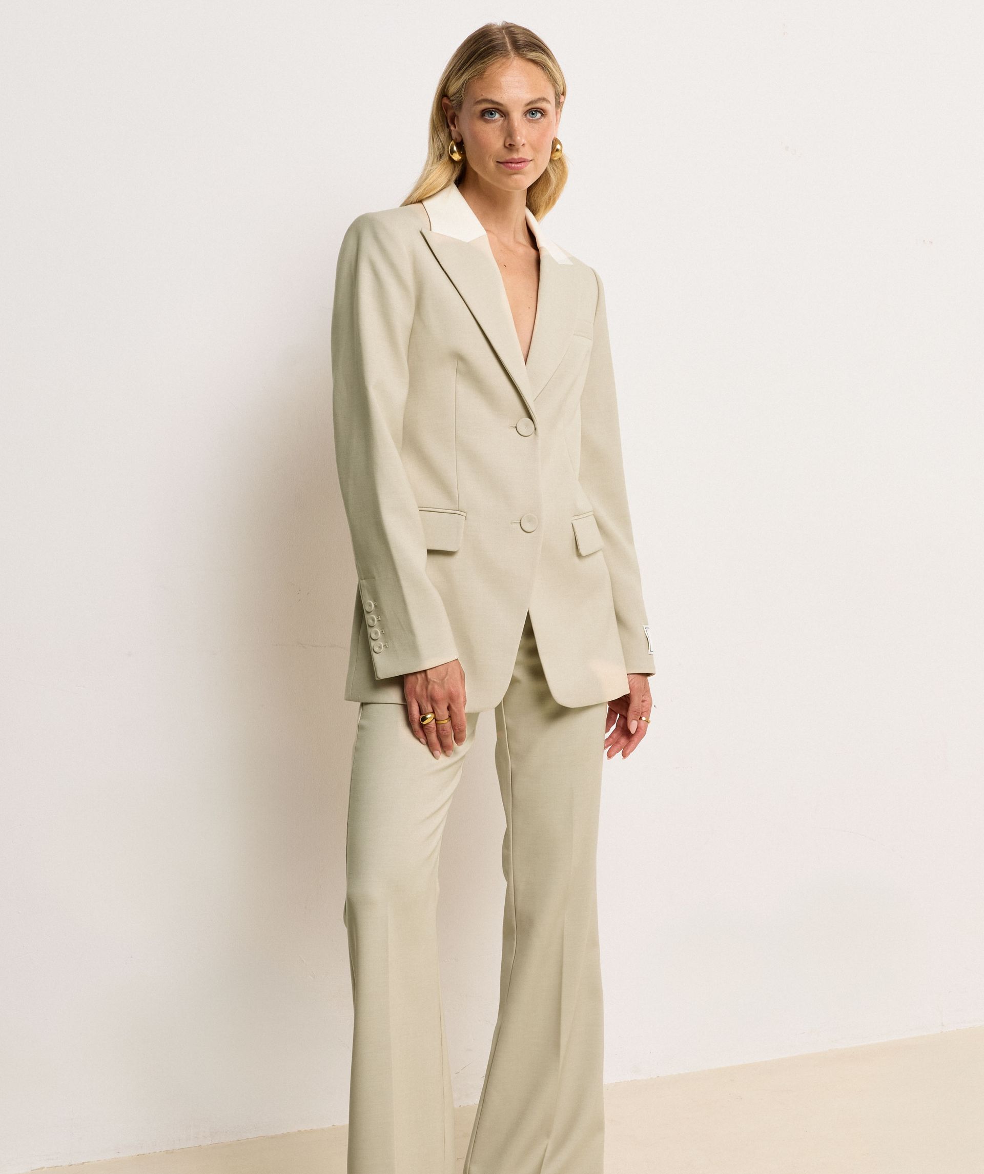 Het model draagt een fitted blazer in de kleur Ecru Melange, waarbij de kraag is uitgevoerd in ecru en de rest van de blazer in melange. Op de mouw is het JOSH V-label te zien