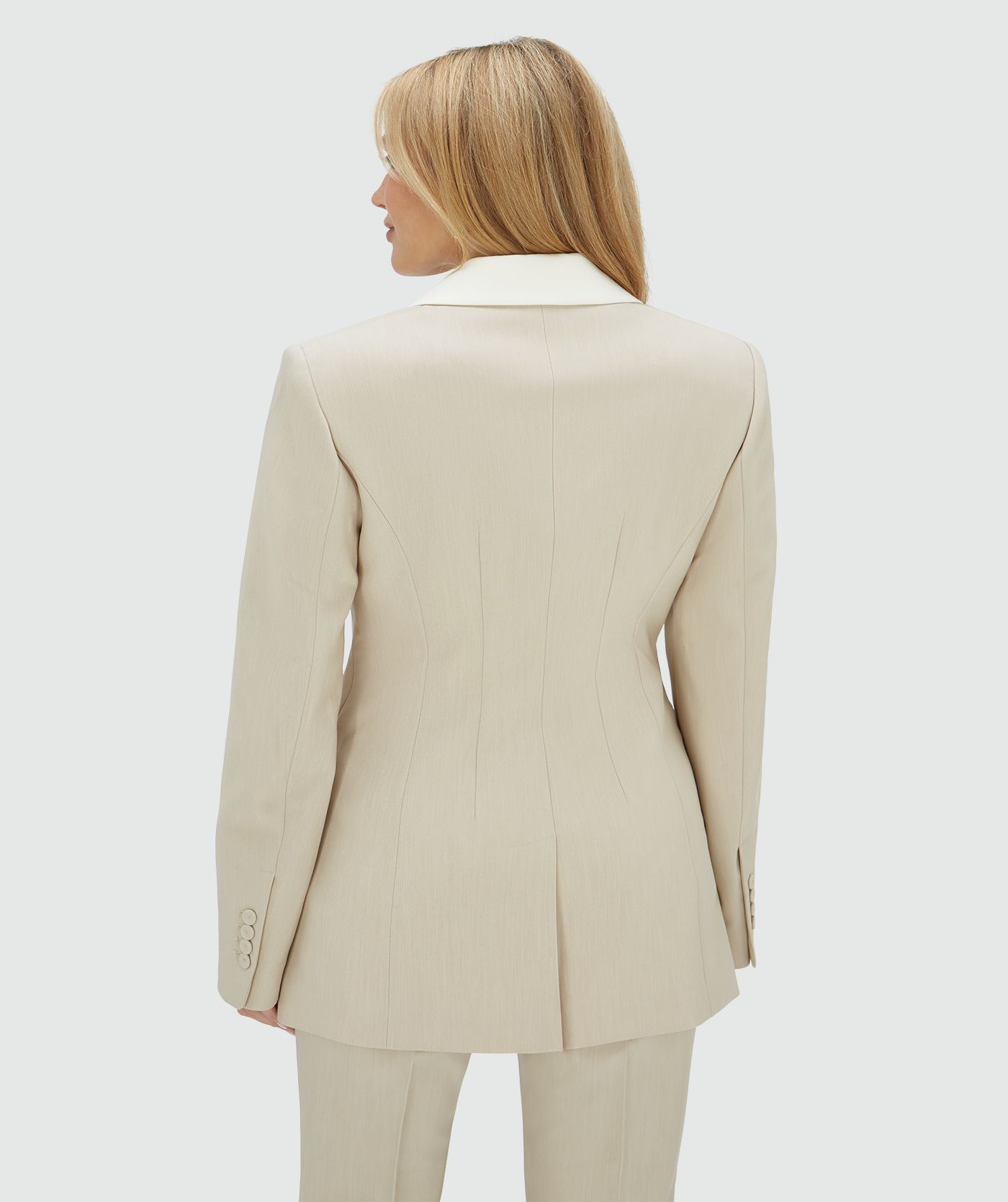Achteraanzicht van het model in een fitted blazer in de kleur Ecru Melange, waarbij de kraag is uitgevoerd in ecru en de rest van de blazer in melange. Op de mouw is het JOSH V-label zichtbaar