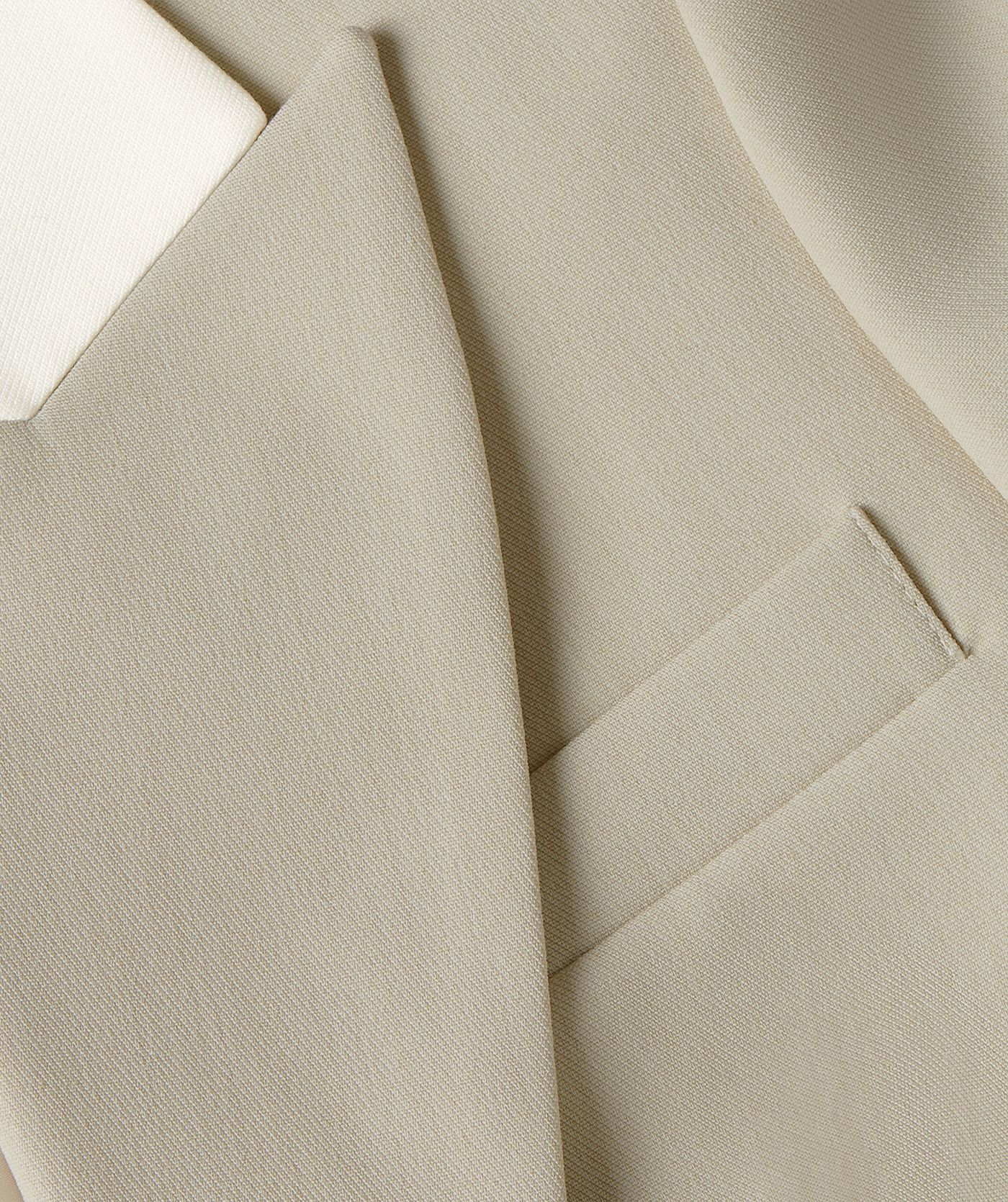 Close-up van een fitted blazer in de kleur Ecru Melange, waarbij de kraag is uitgevoerd in ecru en de rest van de blazer in melange. In beeld is de paspelzak aan de voorzijde zichtbaar