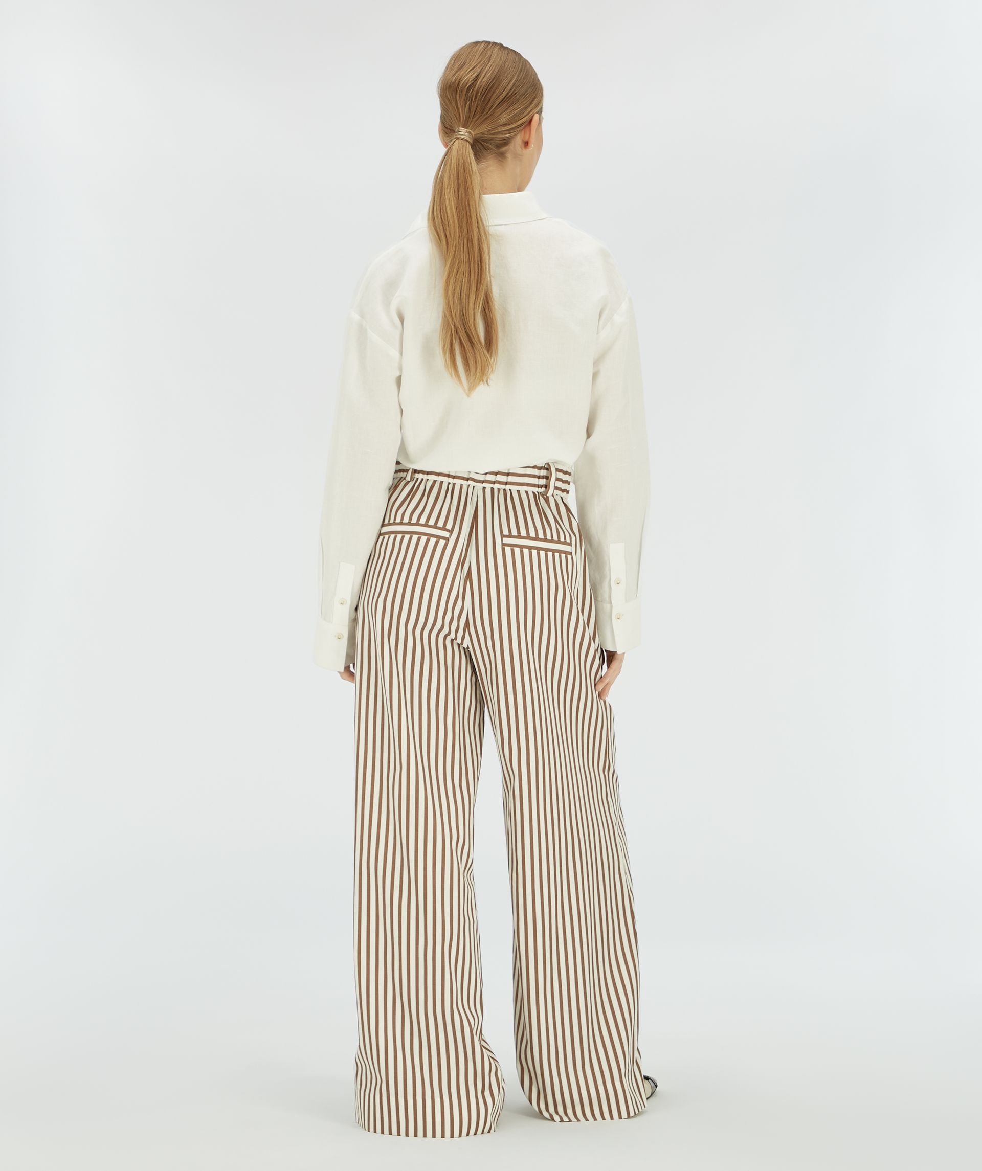 Achteraanzicht van model in een bruin wit gestreepte broek.