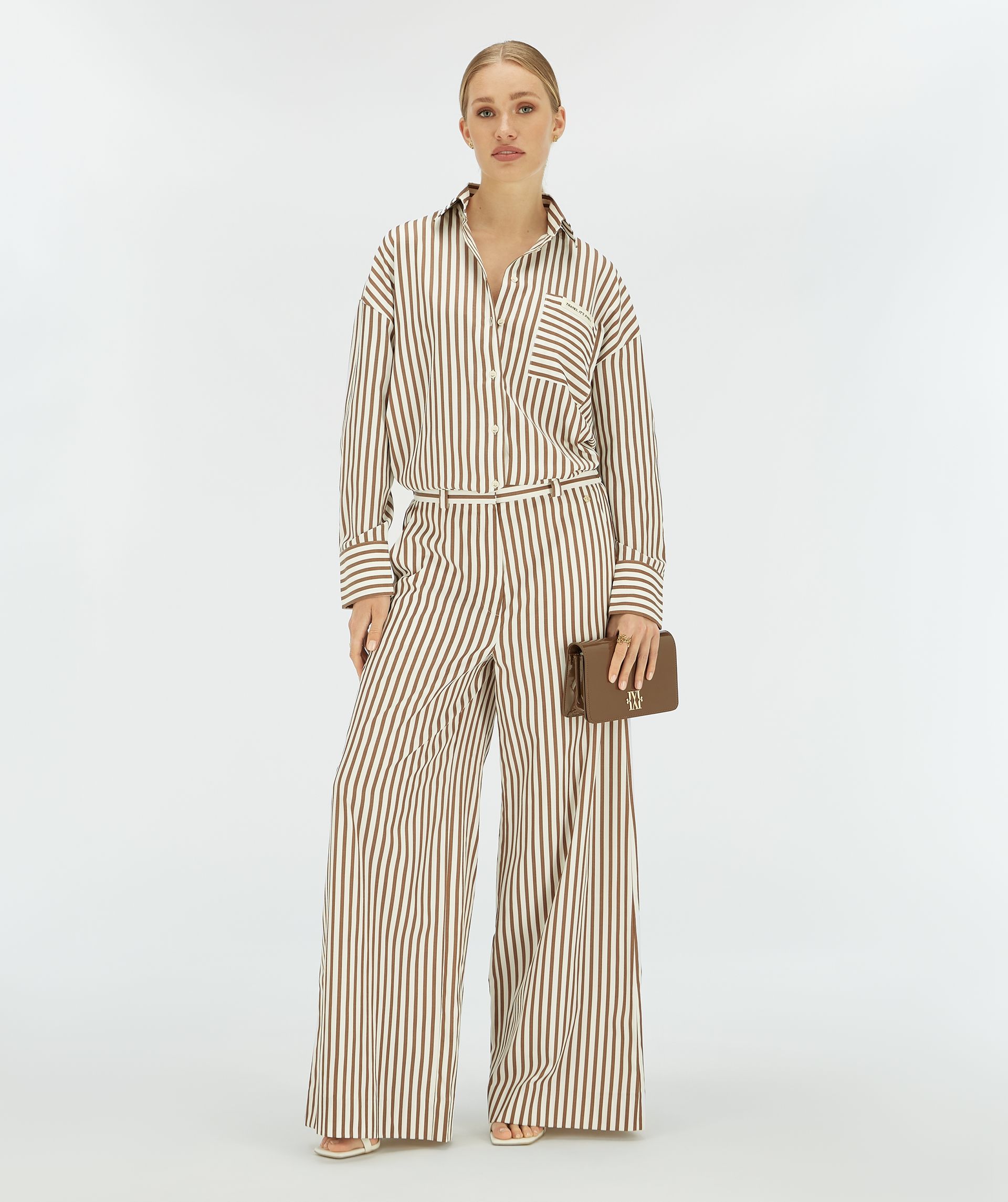 Model draagt een bruin wit gestreepte wide leg broek,.