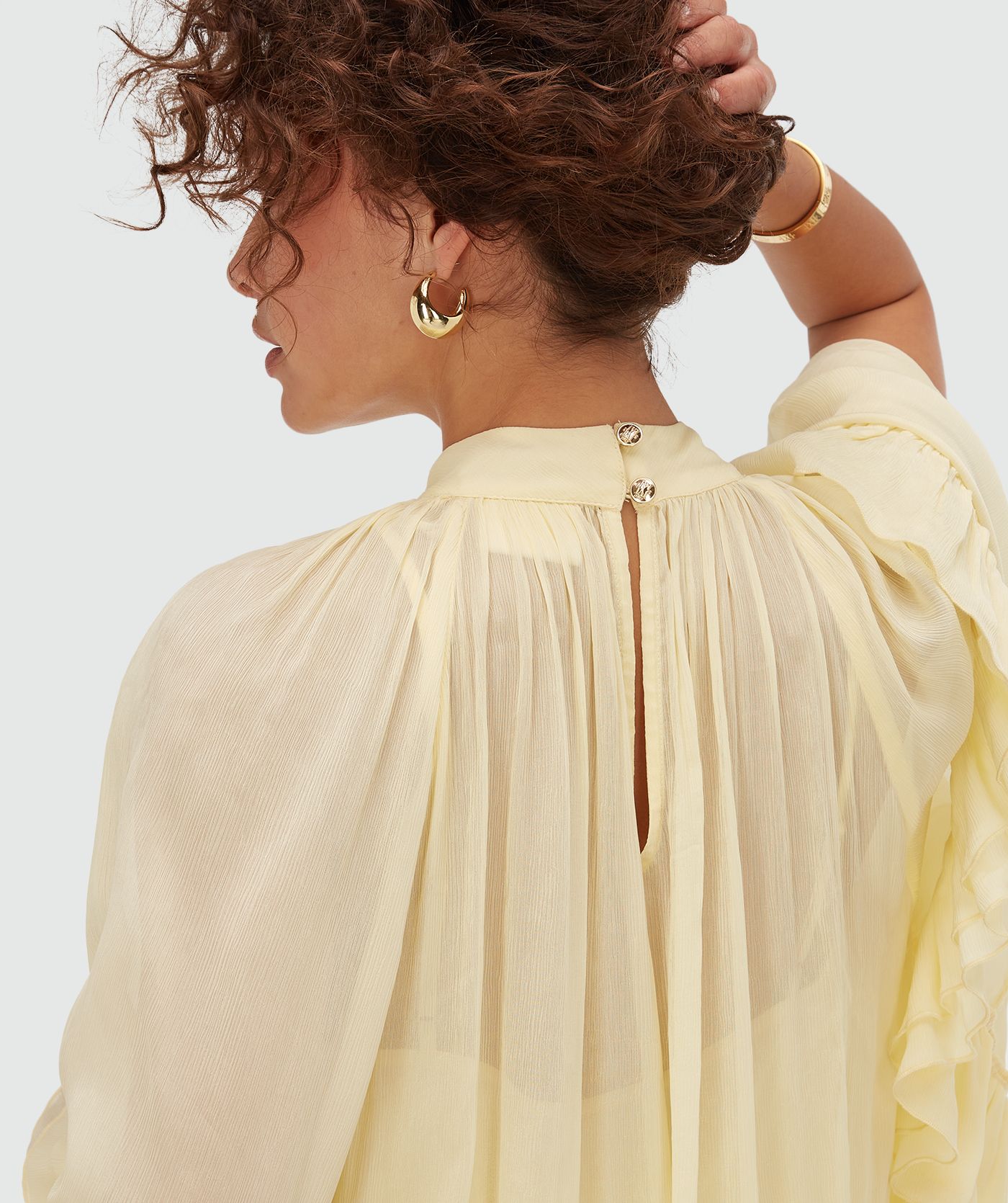 Achterzijde close-up van sluiting model in een oversized top met ruffle details in de kleur Butter Yellow