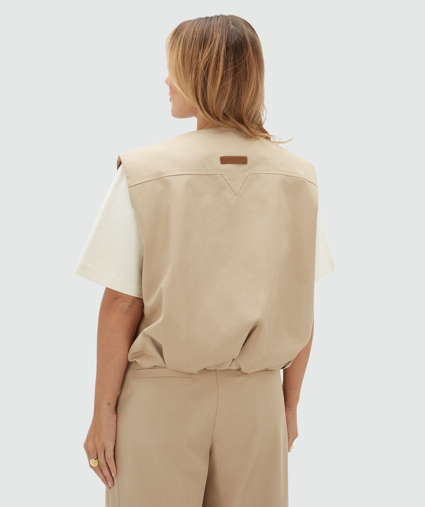 Achteraanzicht van een model in een beige gilet met een leren detail op de rug.