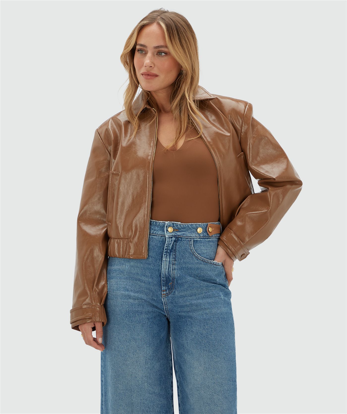 Model draagt een cognac kleurig lak look jasje met rits op een jeans.