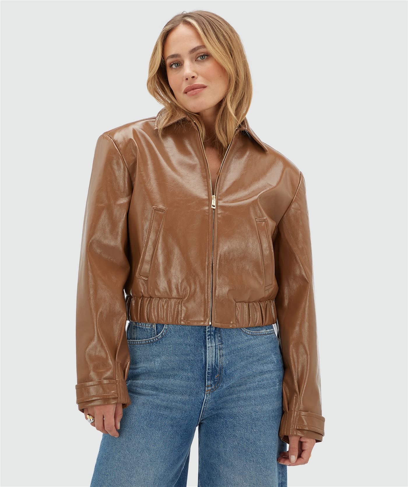 Model draagt een cognac kleurig lak look jasje met rits op een jeans.