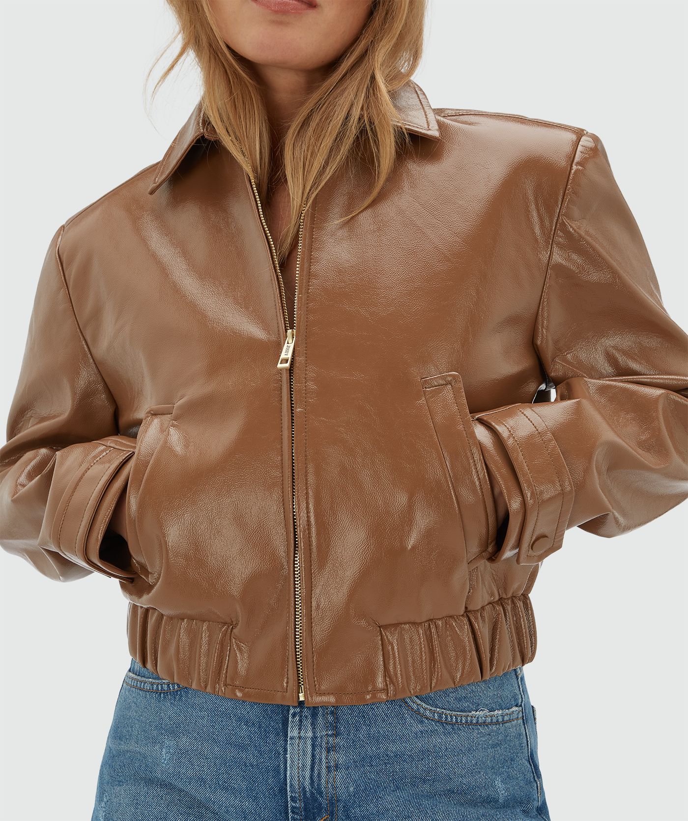 Model draagt een cognac kleurig lak look jasje met rits op een jeans.