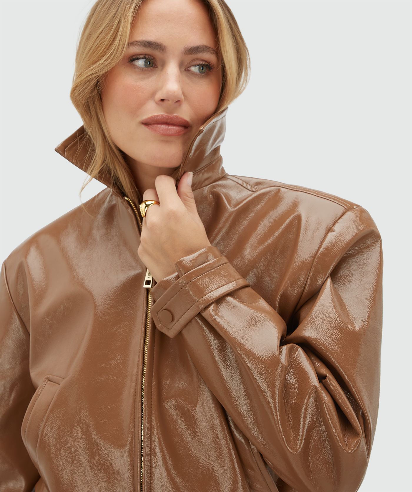 Model draagt een cognac kleurig lak look jasje met rits op een jeans.