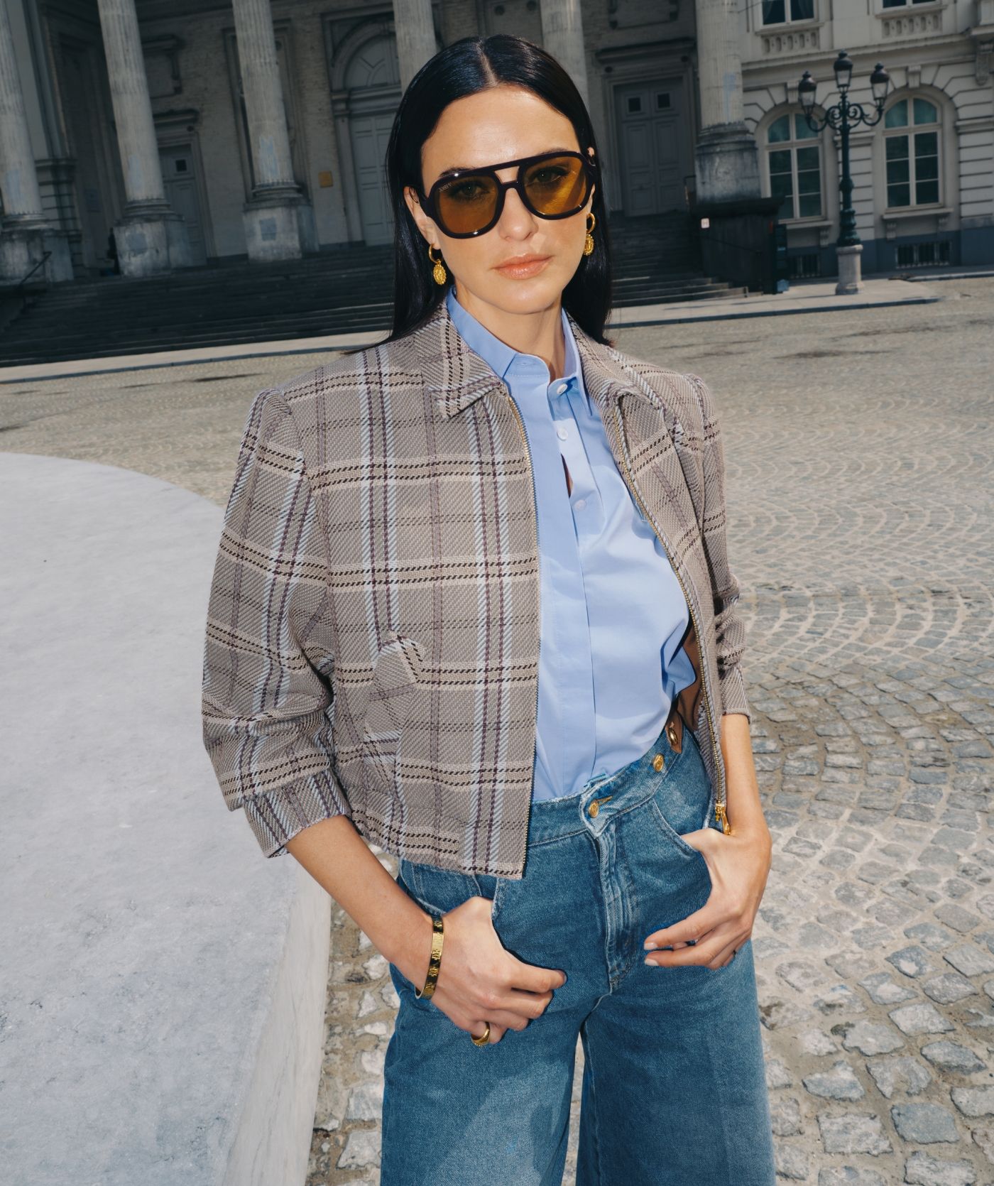 Model draagt een geruit jasje met een lichtblauwe blouse en een jeans.