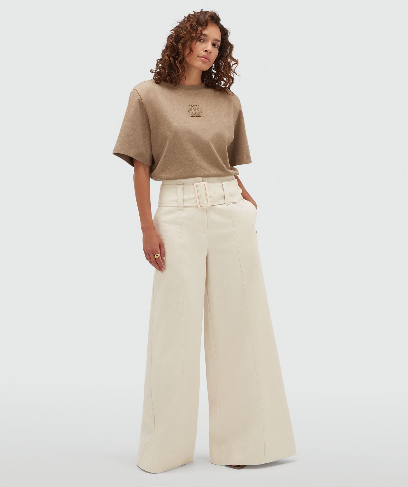 Model draagt een bruine T-shirt body gecombineerd met een gebroken witte broek.