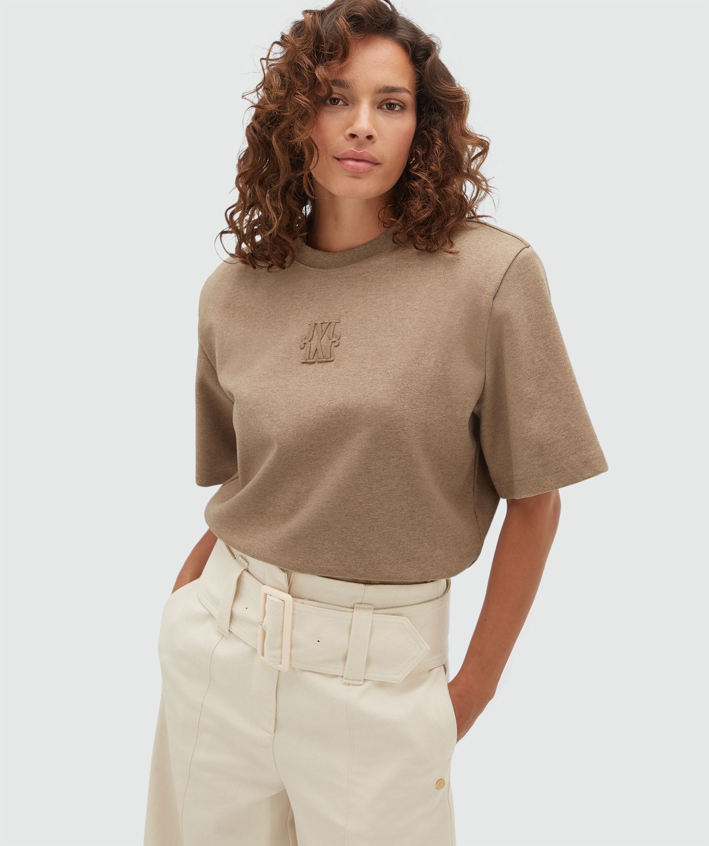 Model draagt een bruine T-shirt body gecombineerd met een gebroken witte broek.