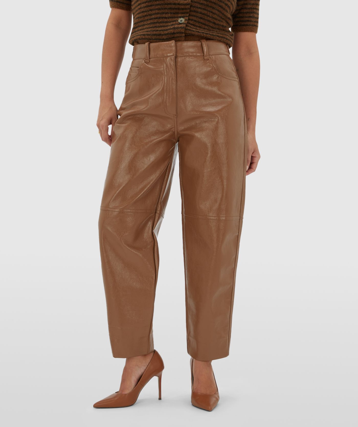 Model draagt een lichtbruine lak look broek gecombineerd met een donkerbruin lichtbruin gestreept vestje met korte mouwen.