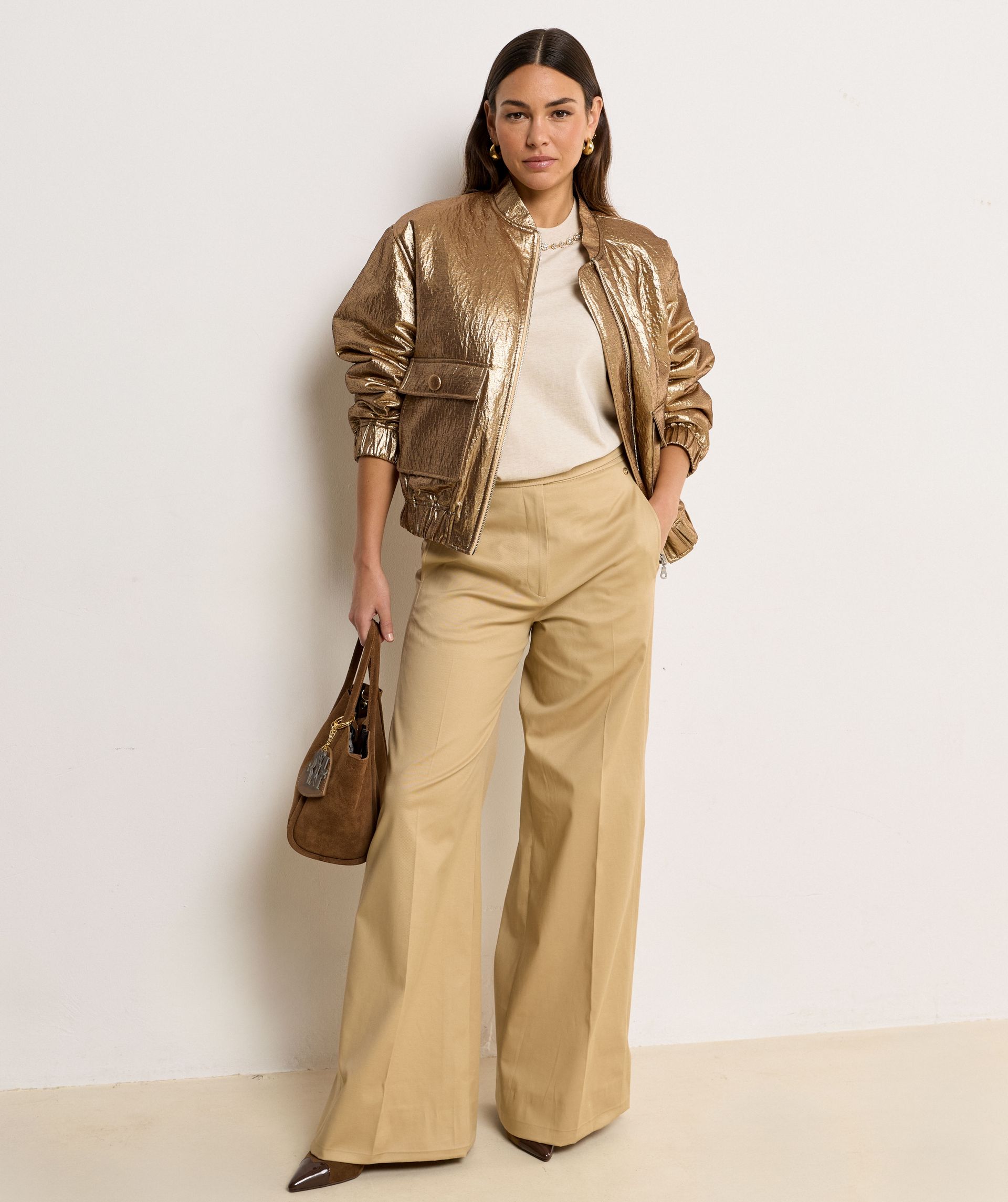 Het model draagt een mid rise wide leg pantalon in de kleur Light Camel, voorzien van verstelbare knopen in de tailleband