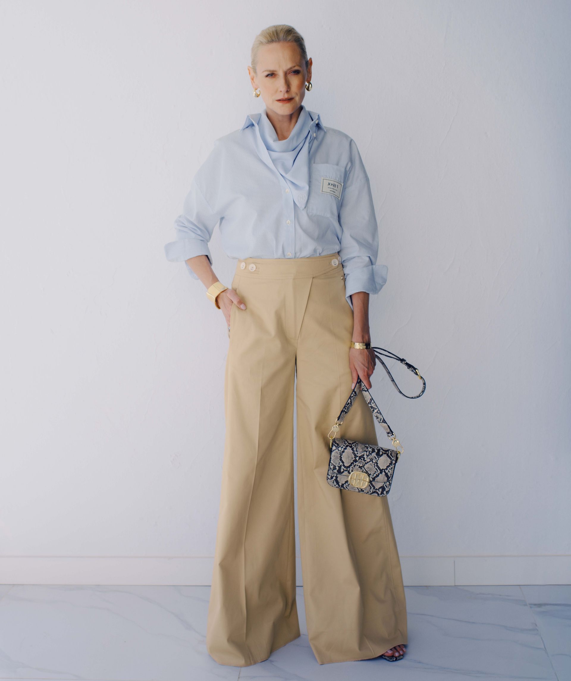 Het model draagt een mid rise wide leg pantalon in de kleur Light Camel, voorzien van verstelbare knopen in de tailleband