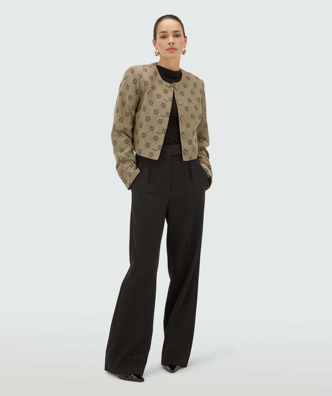 Model draagt een Beige Black blazer met een all-over jacquard geweven logopatroon, schoudervullingen en valt cropped - Josh V