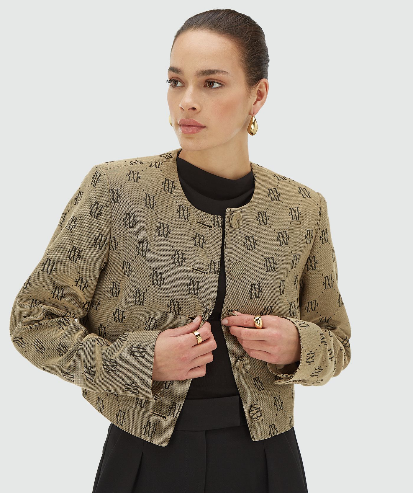 Model draagt een Beige Black blazer met een all-over jacquard geweven logopatroon, schoudervullingen en valt cropped - Josh V