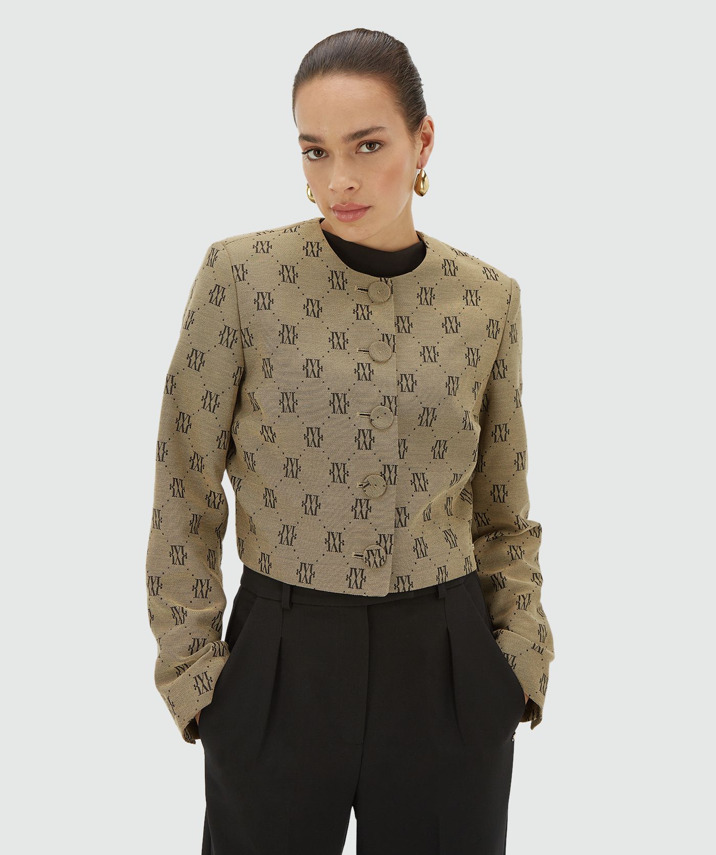 Model draagt een Beige Black blazer met een all-over jacquard geweven logopatroon, schoudervullingen en valt cropped - Josh V