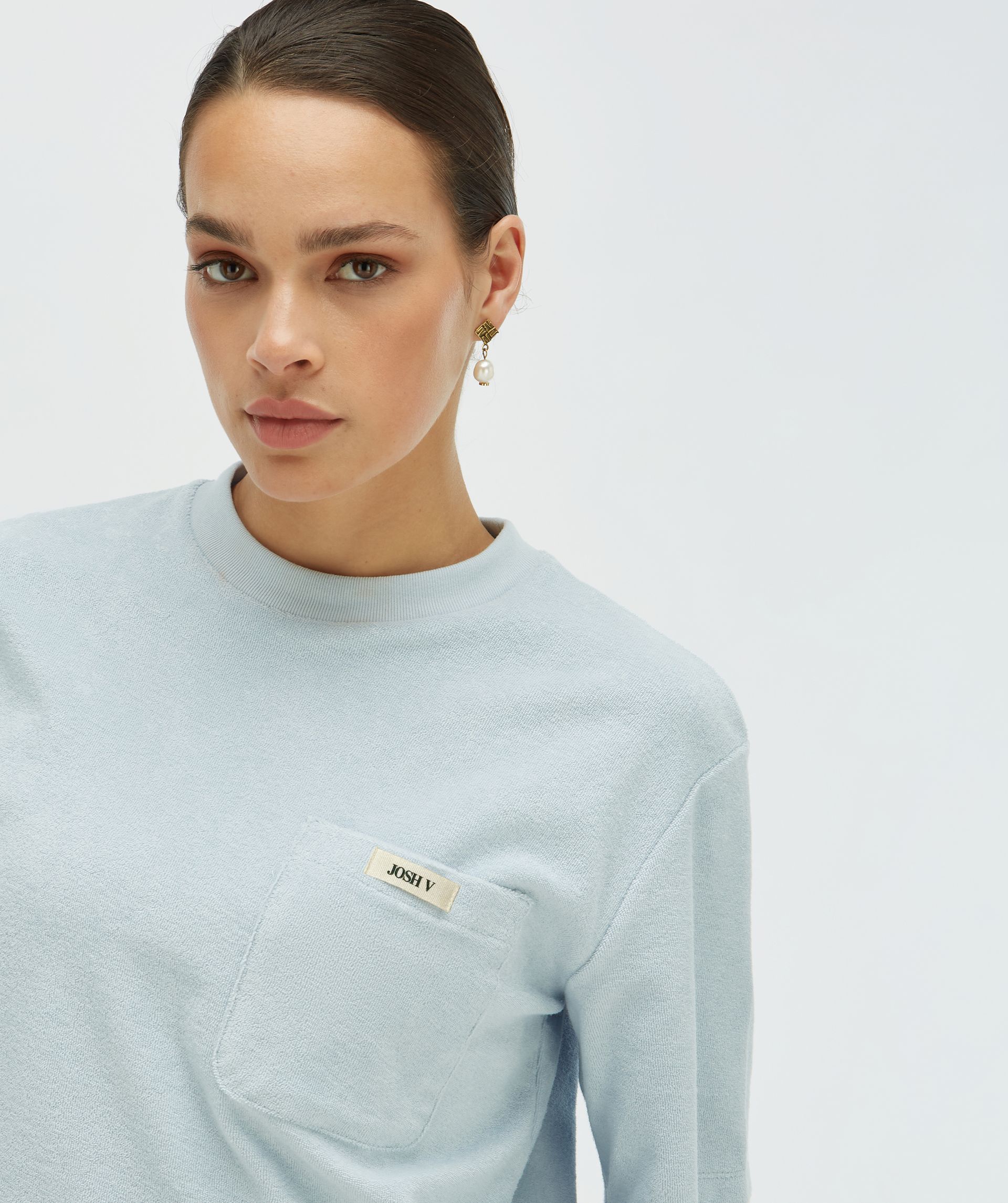 Model draagt een oversized T-shirt in de kleur lichtblauw met een borstzak voorzien van het JOSH V-logo - Josh V.