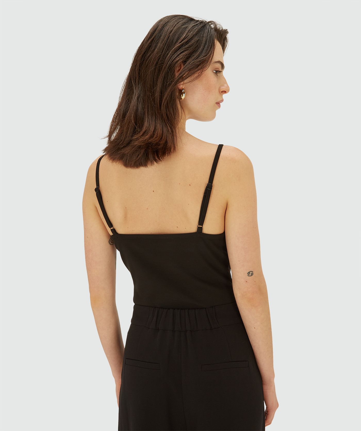 Achteraanzicht van model in een zwarte sleeveless jersey top met dunne bandjes en een V-hals afgewerkt met kant. De top heeft een subtiel logo aan de voorzijde