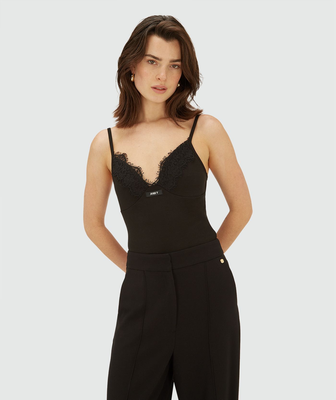 Model draagt een zwarte sleeveless jersey top met dunne bandjes en een V-hals afgewerkt met kant. De top heeft een subtiel logo aan de voorzijde
