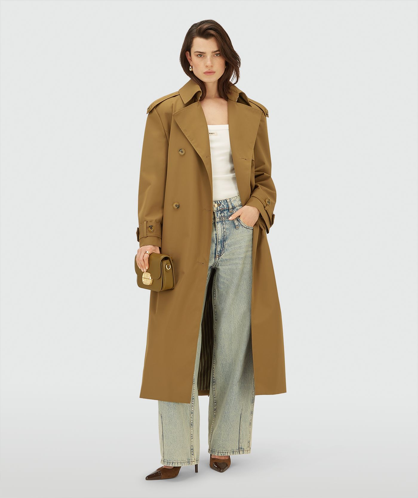 Model draagt een lange, Mid Brown trenchcoat met dubbele knopen en ceintuur in de taille