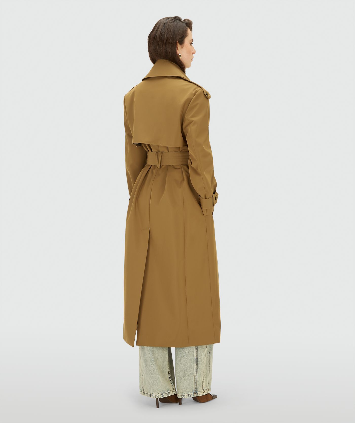 Achteraanzicht van een model in een lange, Mid Brown trenchcoat met dubbele knopen en ceintuur in de taille