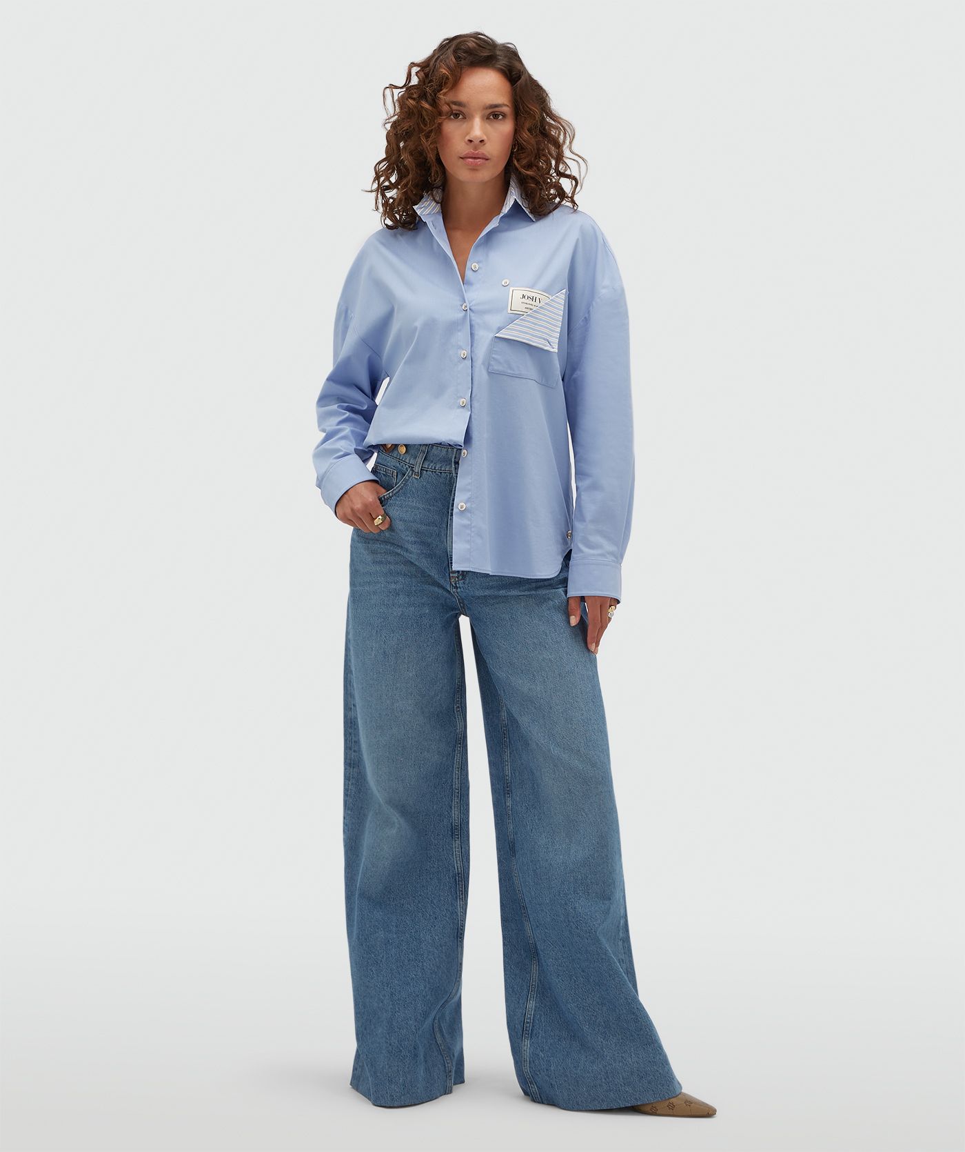 Model draagt een lichtblauwe oversized blouse met een opengevouwen borstzak waar een JOSH V-label zichtbaar is.