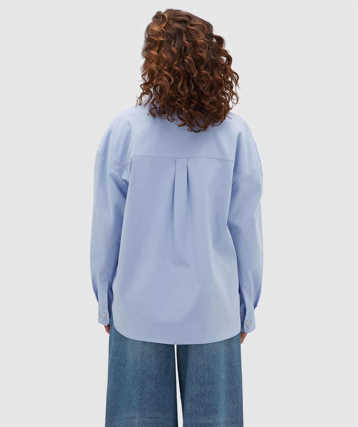 Achteraanzicht van een model in een lichtblauwe oversized blouse.