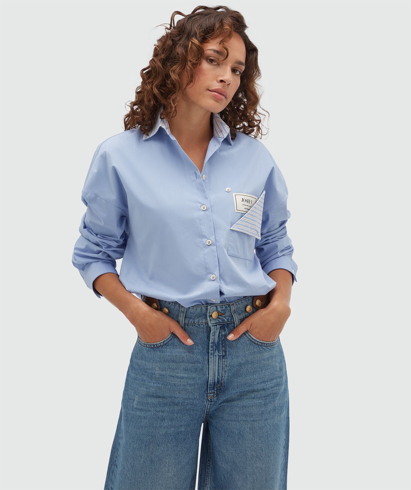 Model draagt een lichtblauwe oversized blouse met een opengevouwen borstzak waar een JOSH V-label zichtbaar is.