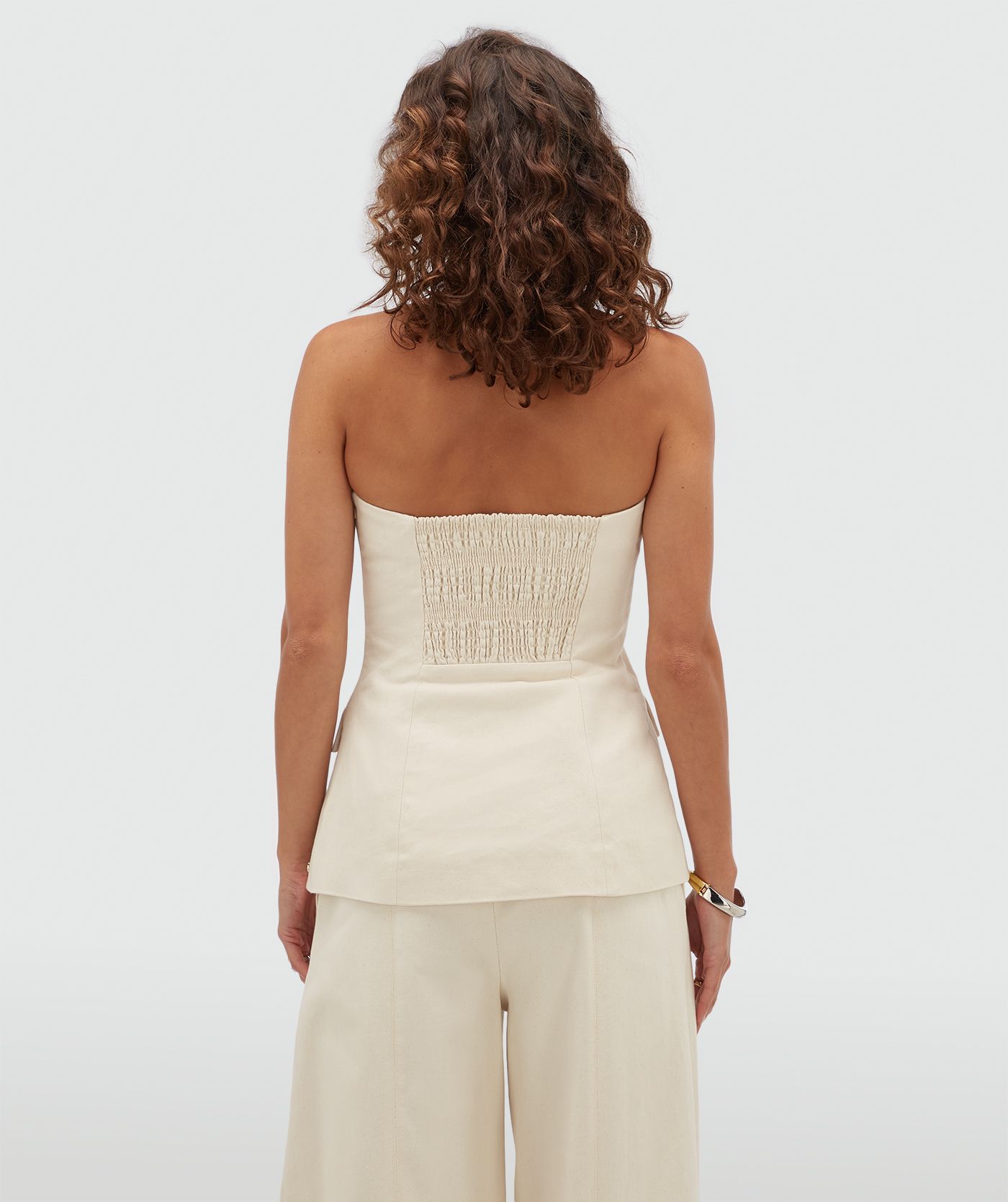Achteraanzicht van een model in een gebroken witte bustier top met elastiek aan de achetrkant.