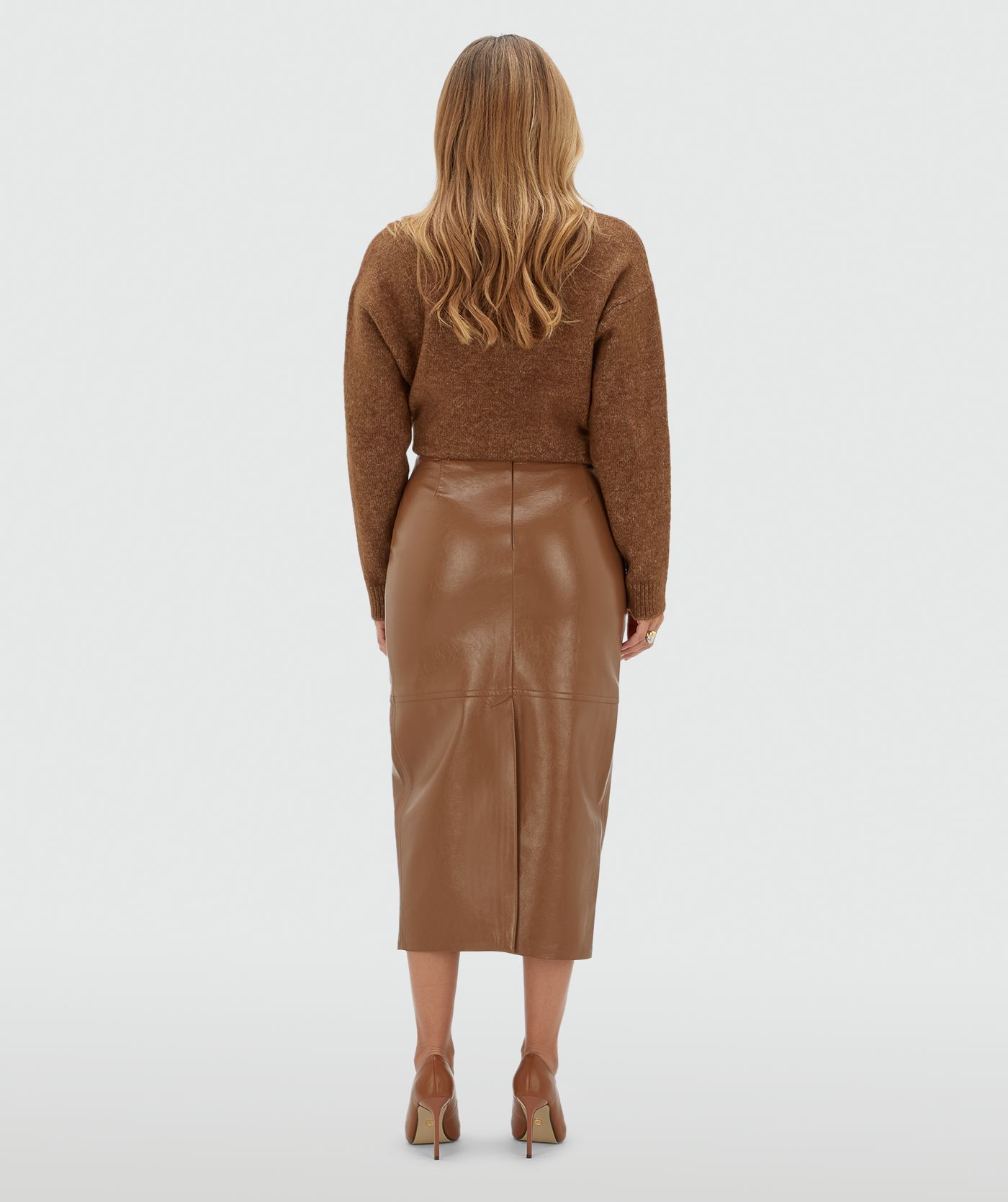 Achteraanzicht van een model in een lange bruine lak look rok met een split aan de achterkant.