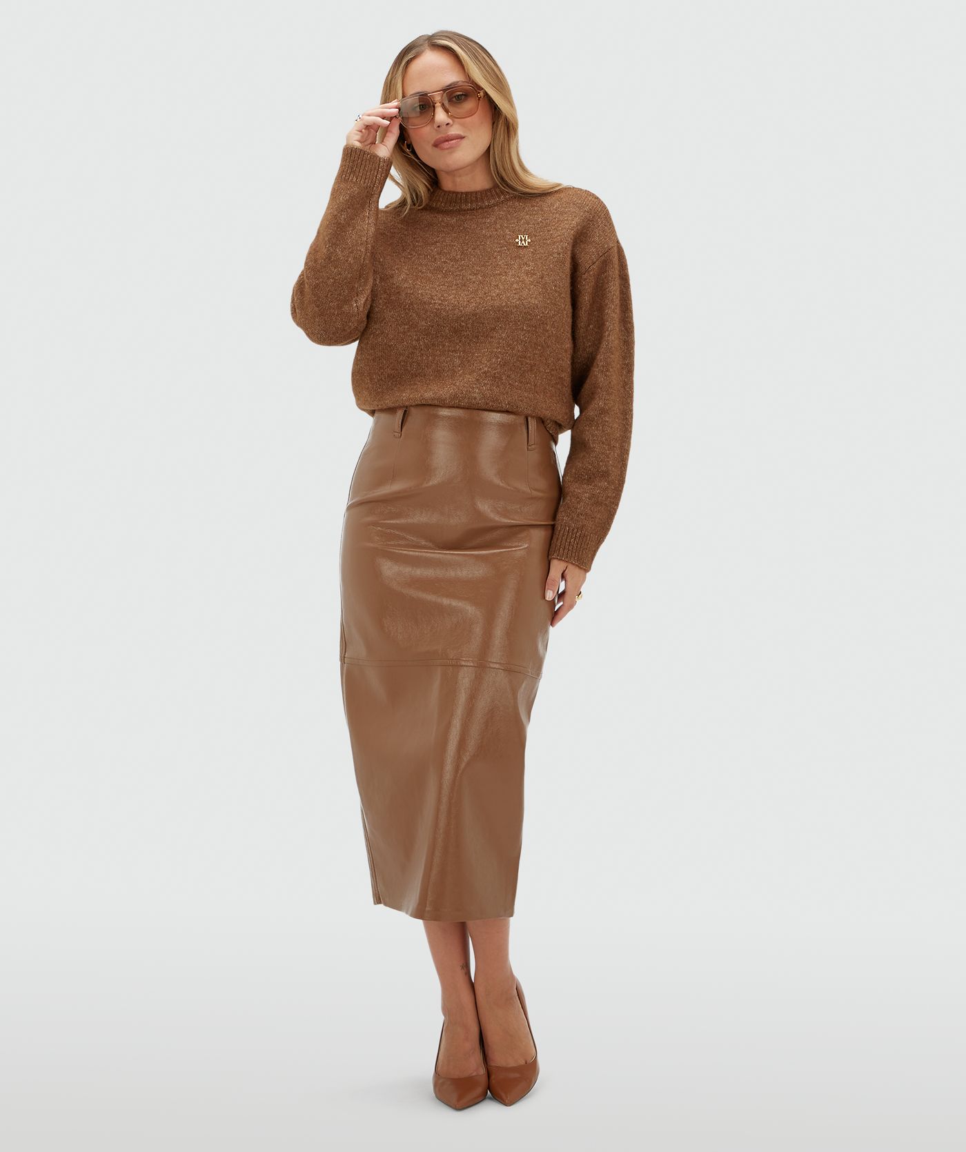Model draagt bruine lange lak look rok gecombineerd met een bruine trui en een riem.